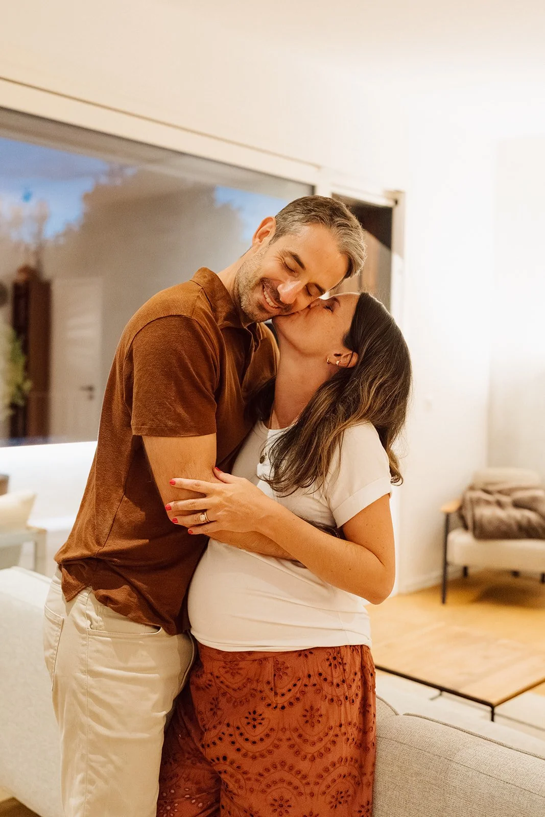 Séance photo grossesse à domicile : un couple s’enlace tendrement dans la douceur de leur intérieur, capturant l’amour et l’attente avant la naissance de leur bébé.