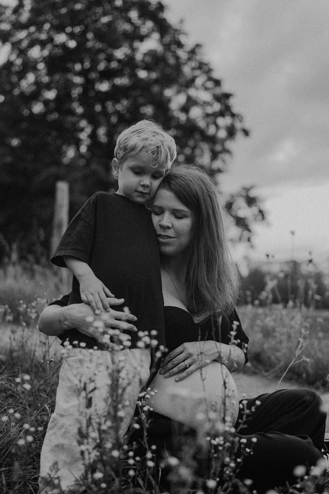 Portrait tendre d’une maman enceinte avec son enfant dans un champ fleuri, capturant un moment de douceur et de complicité avant l’arrivée du bébé.