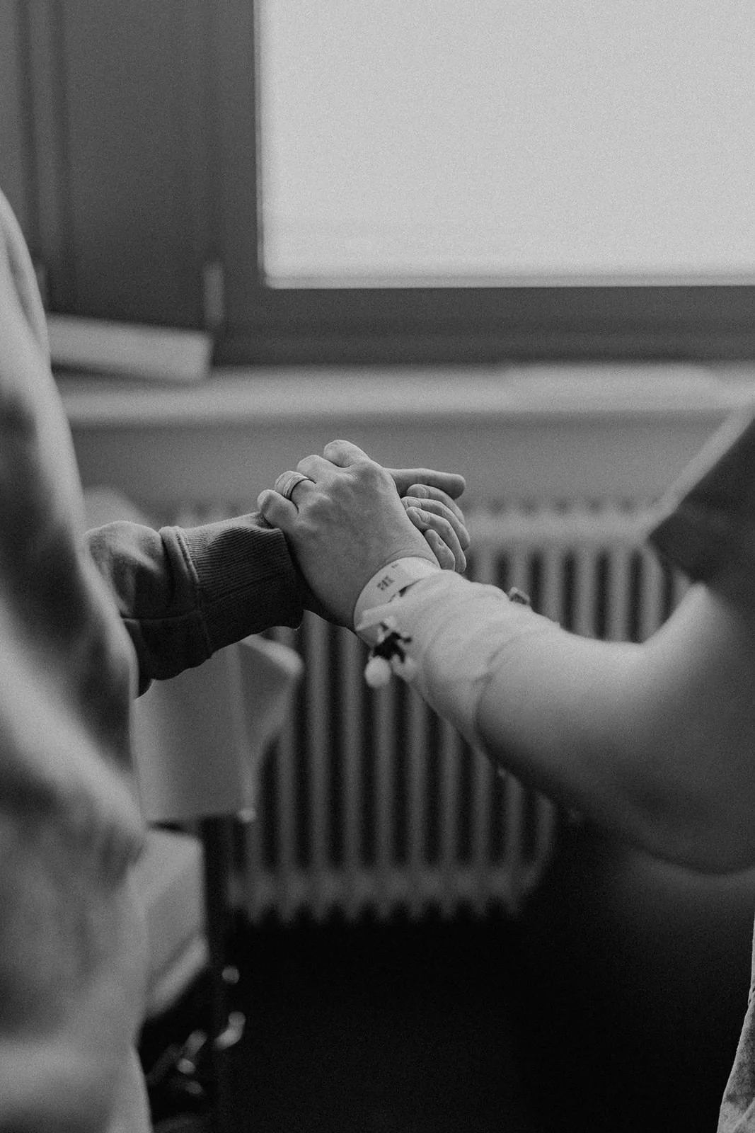 Mains des parents unies pendant le travail en salle de naissance, capturant un geste de soutien et de connexion lors d’un reportage d’accouchement en Suisse romande.