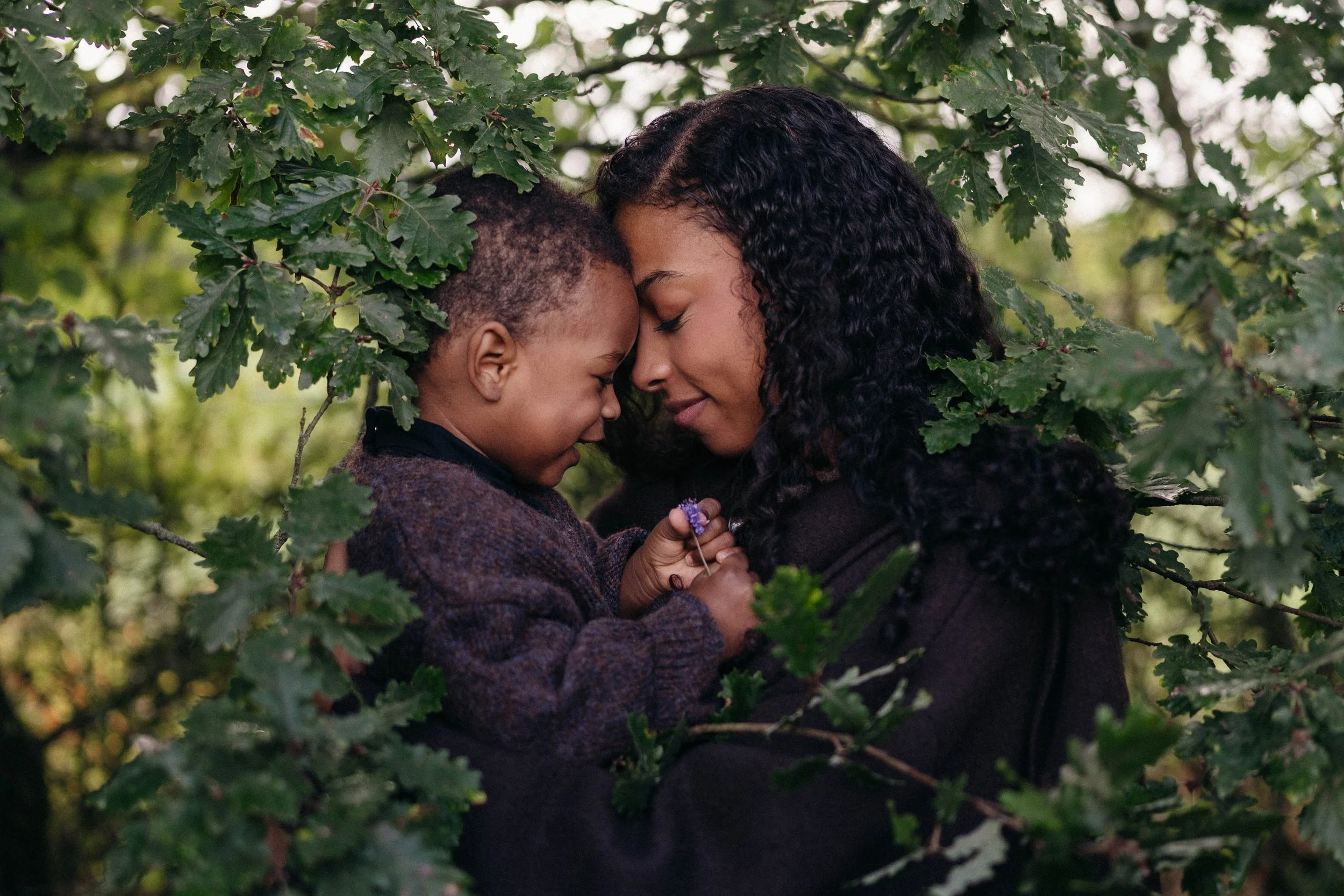 Moment de tendresse entre une mère et son enfant au cœur de la nature, capturé dans un décor végétal intime et poétique lors d’une séance famille lifestyle par Nonante Émotions.