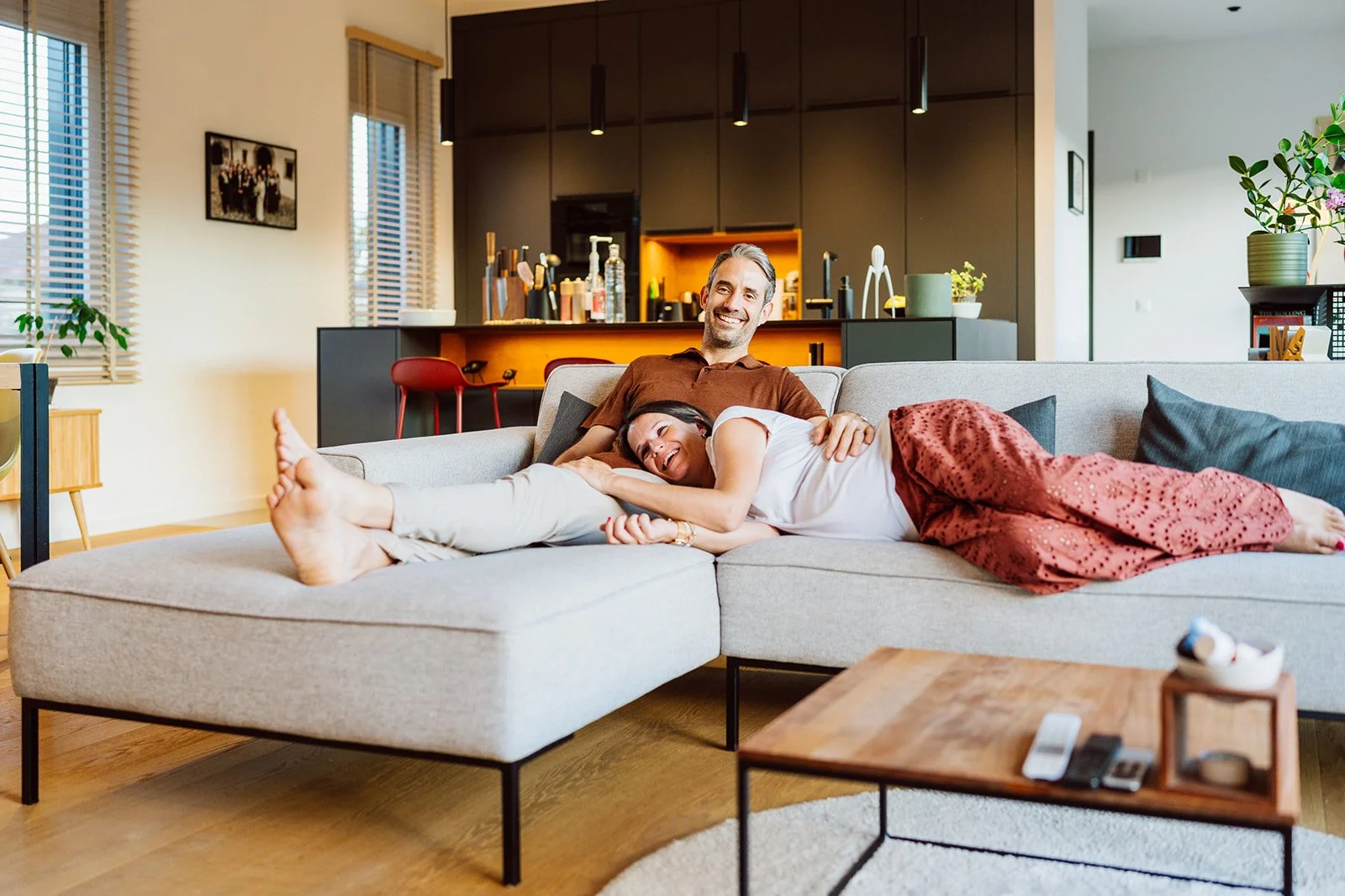 Séance photo grossesse à domicile : un couple partage un moment complice et détendu sur leur canapé, dans l’intimité chaleureuse de leur maison avant l’arrivée de leur bébé.