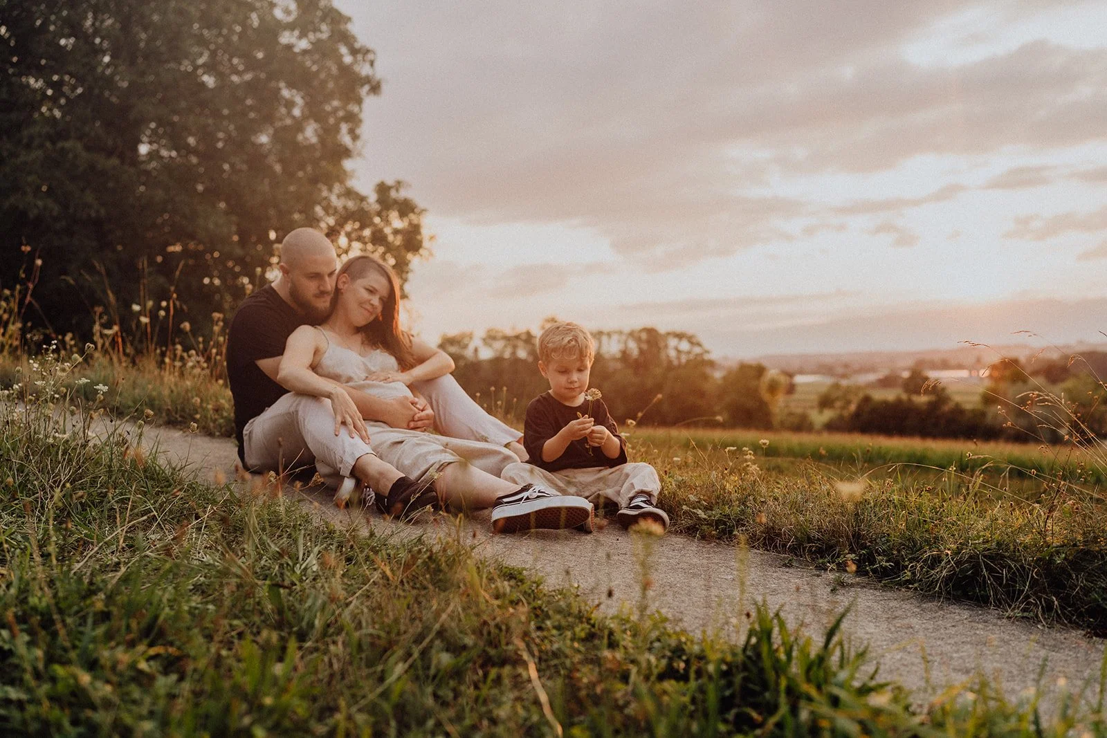 Séance photo maternité en famille au coucher du soleil : parents et enfant partagent un moment paisible dans la nature, avant l’arrivée du nouveau bébé.