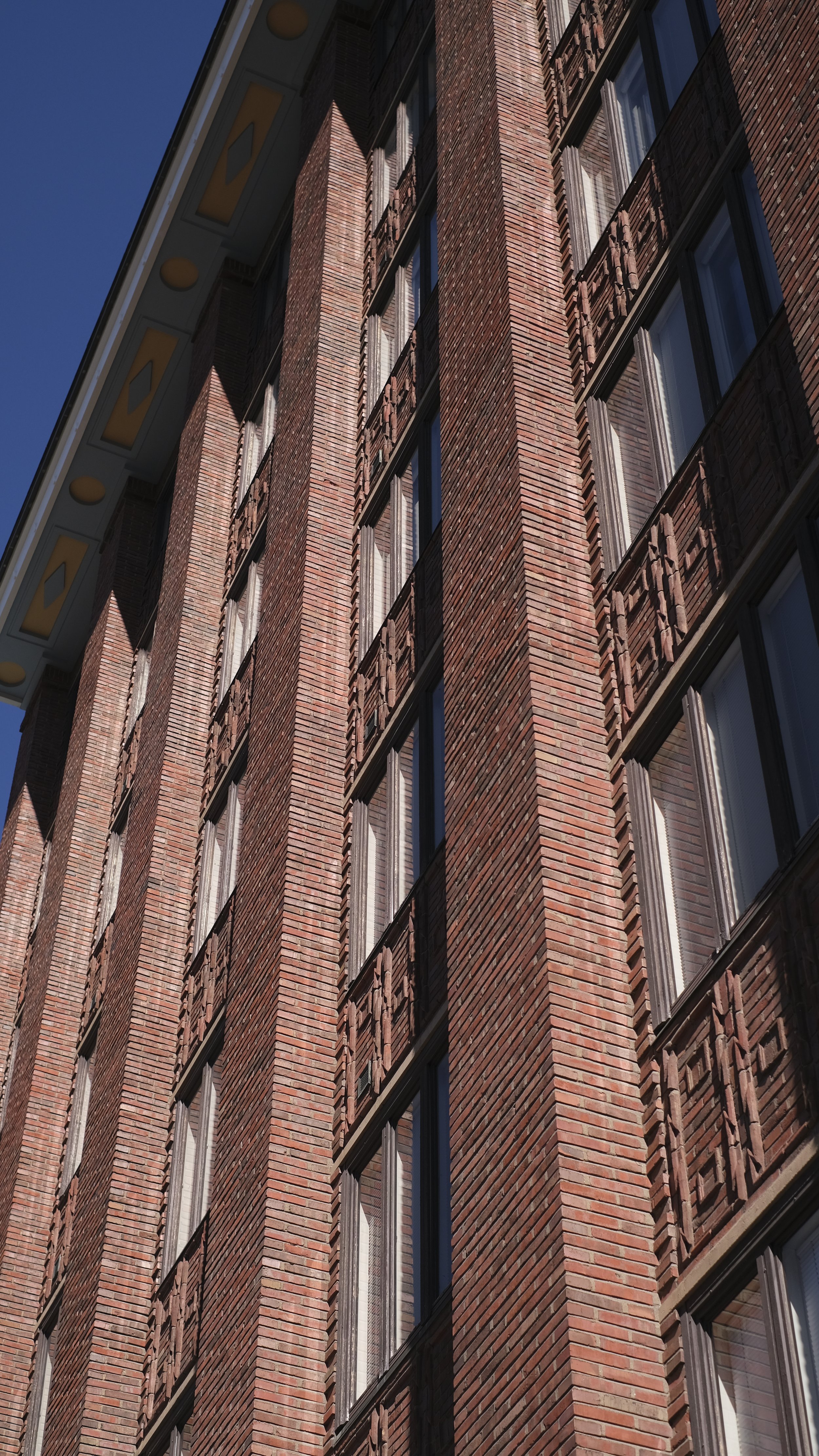 Fara Manuel Photography Helsinki Close-up of a tall brick building with multiple windows, some with curtains, under a clear blue sky.
