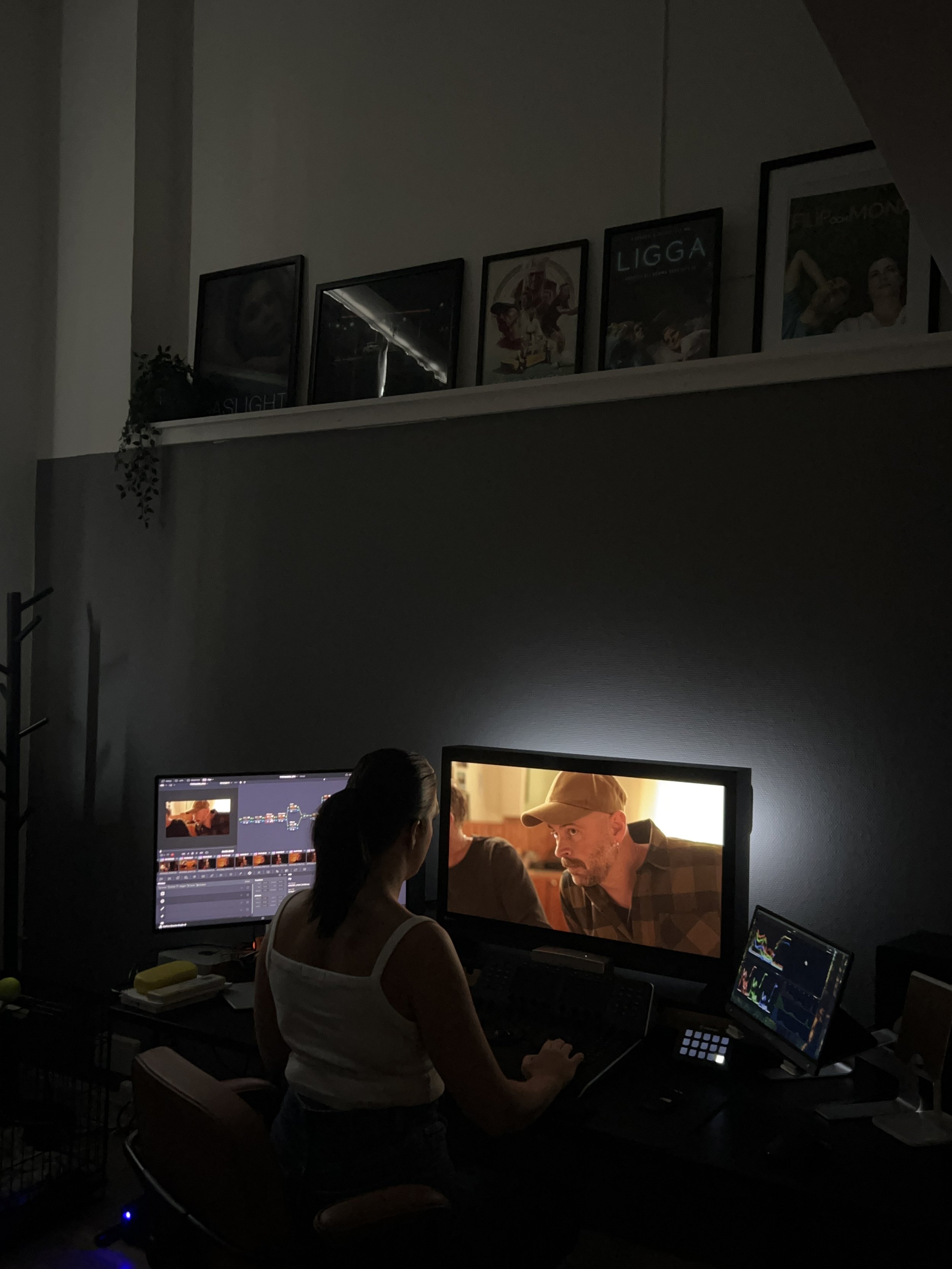A female colorist working with color grading at her computer desk in a her suite, with multiple monitors showing video editing software and a scene from a film.