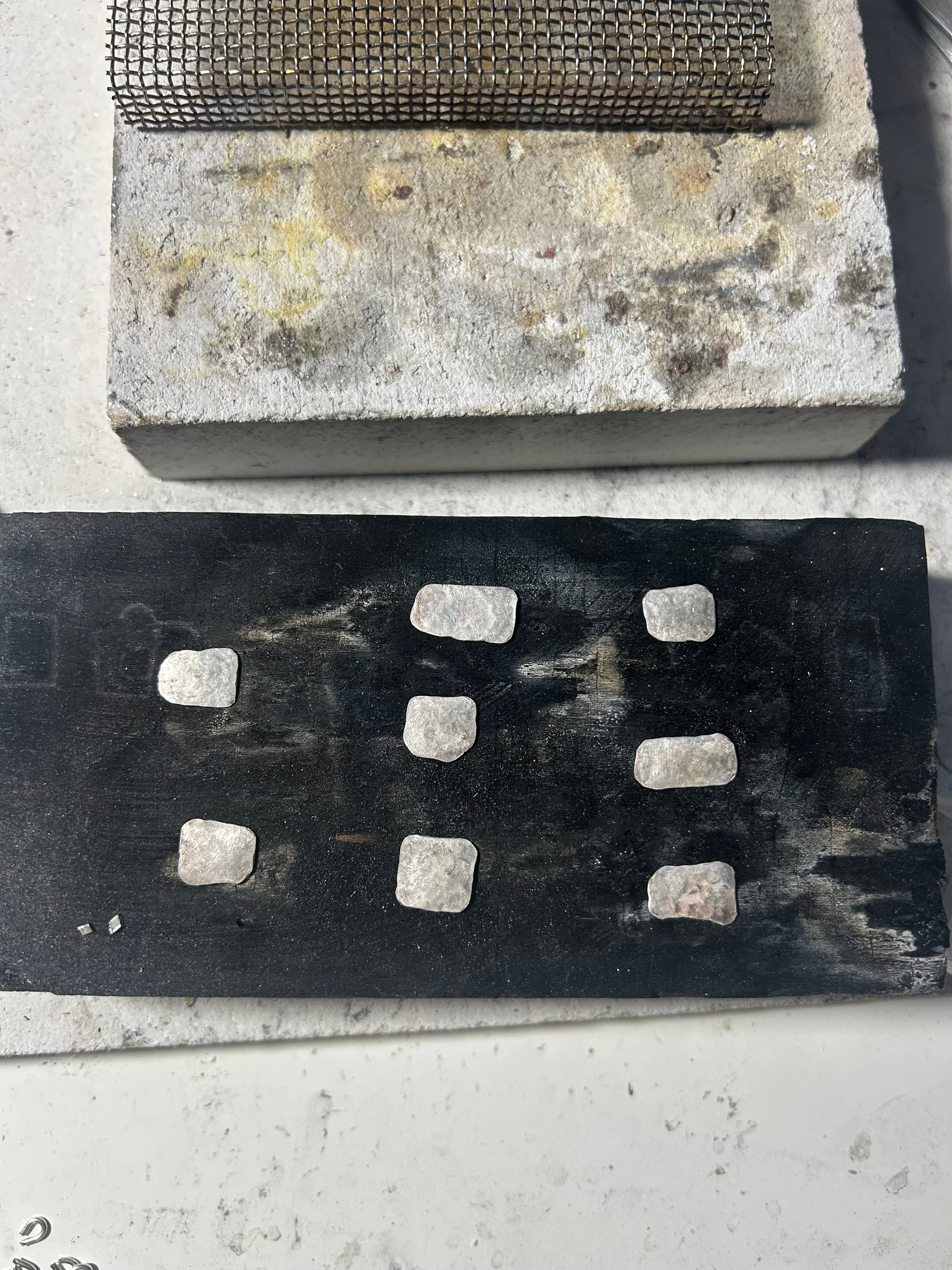 Close-up of a concrete block with a metal mesh on top, placed on a black surface with metal clips underneath, in an industrial setting.
