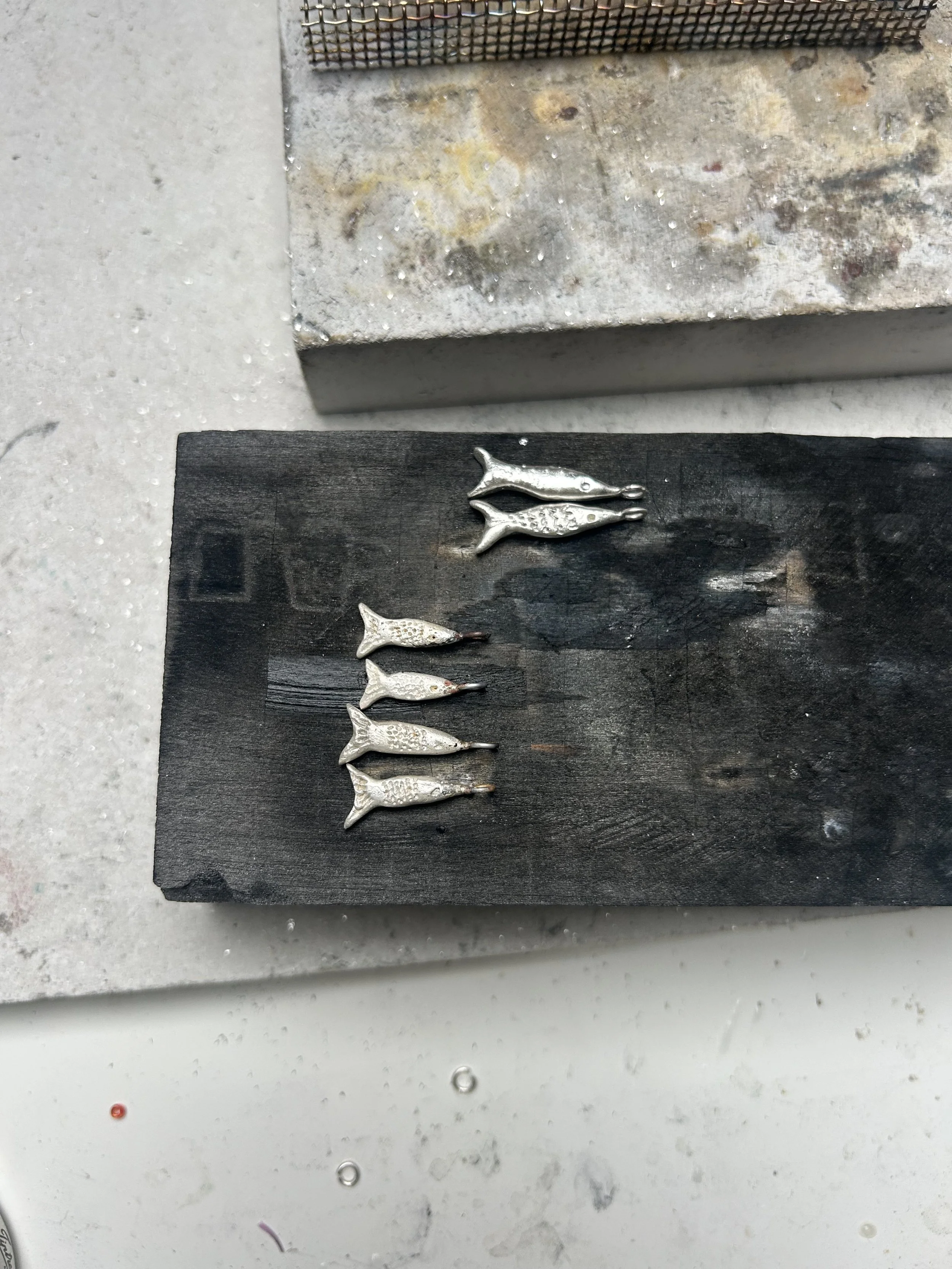 Several small 925 silver fish arranged in a row on a black wooden surface.