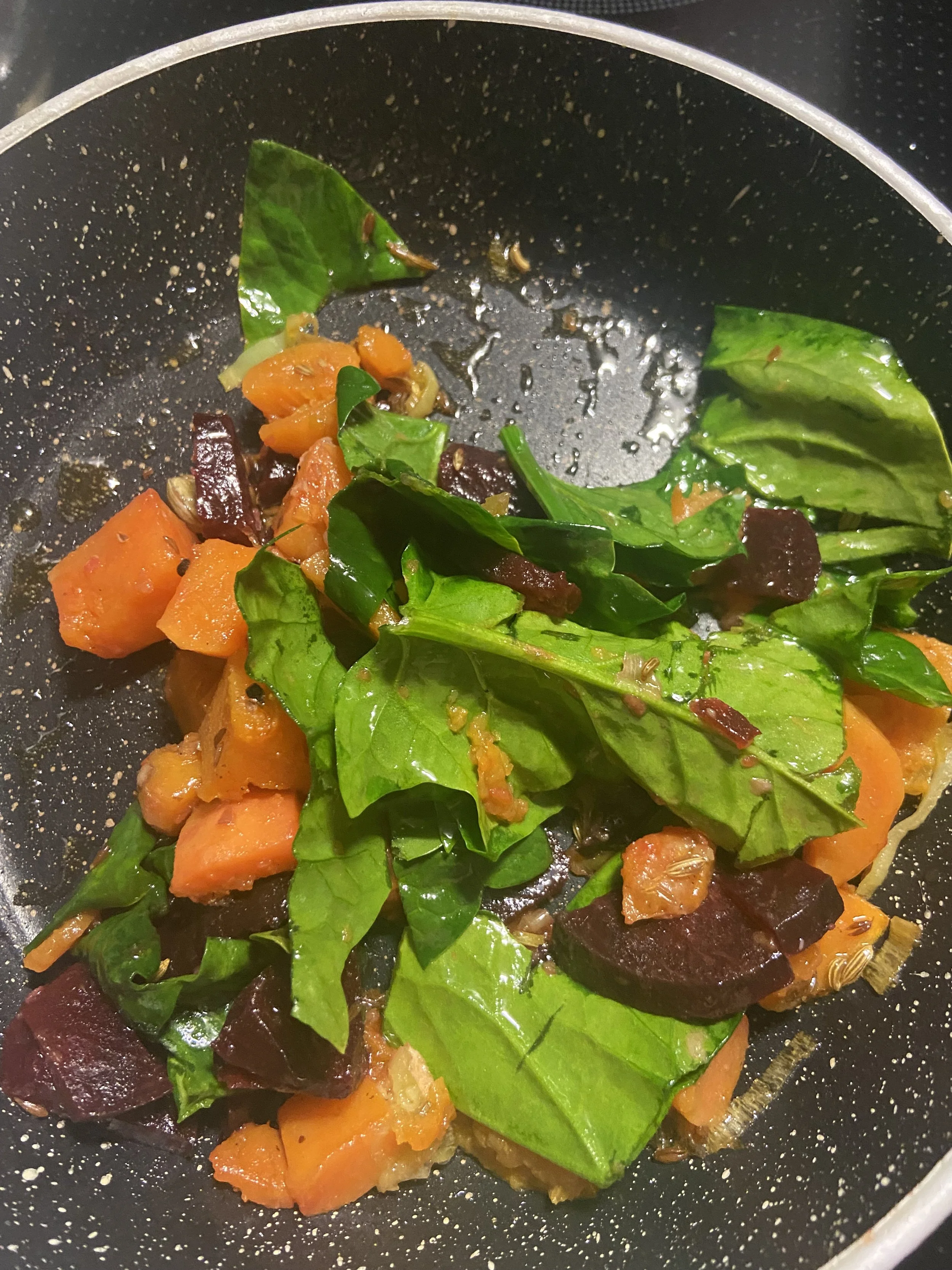 Verduras cocinándose en una sartén, incluyendo hojas verdes, zanahorias y remolacha.