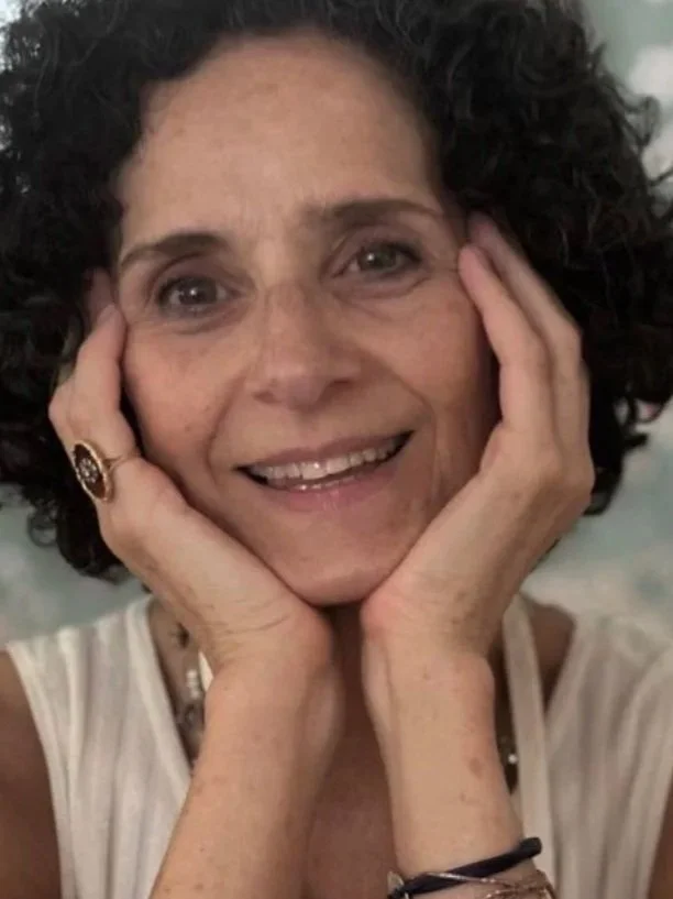 Mujer con cabello rizado, sonriendo y sosteniendo su rostro con las manos.