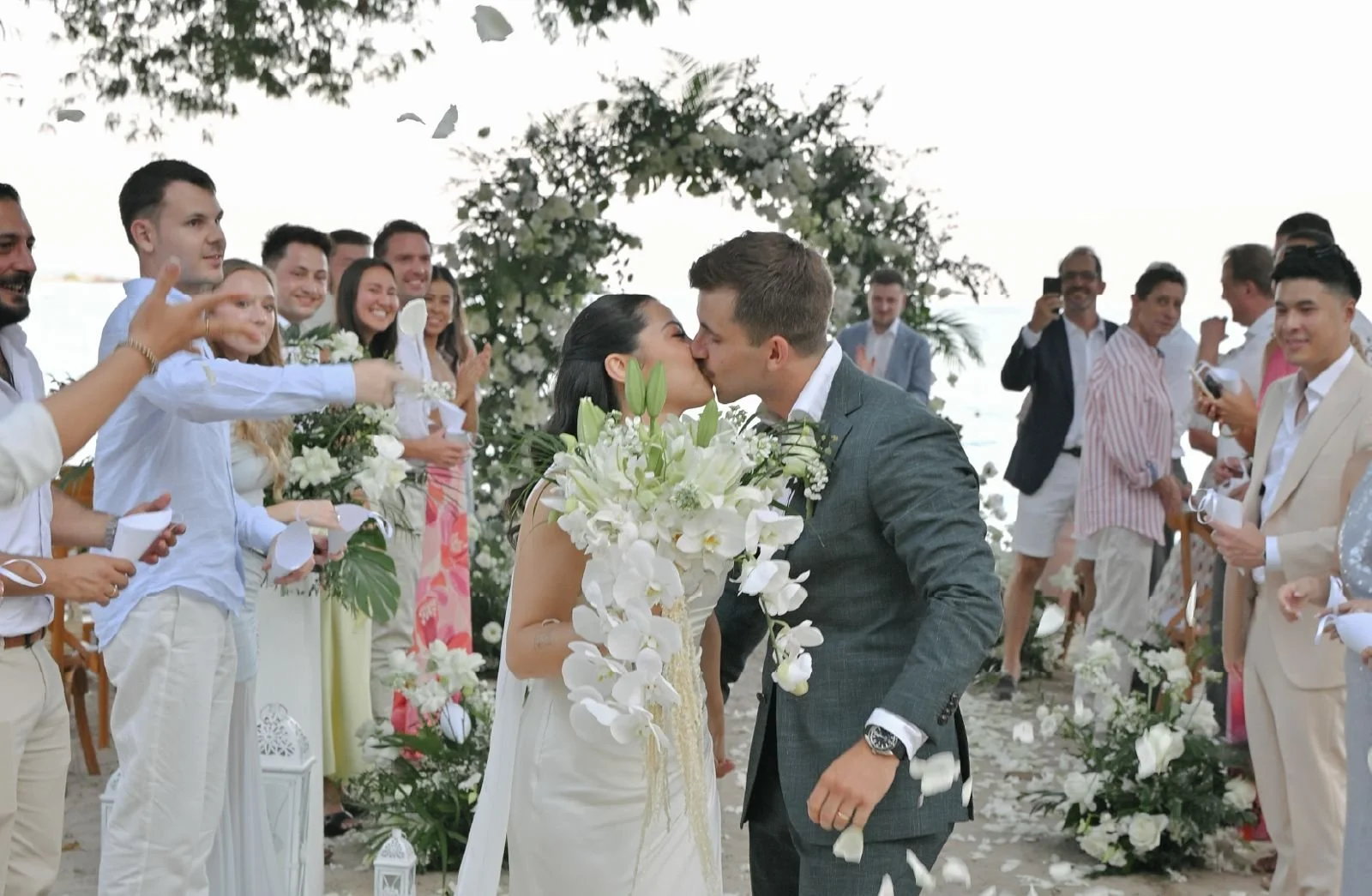 Couple embracing at a sunset beach wedding in Phuket on a private island with guests celebrating in the background
