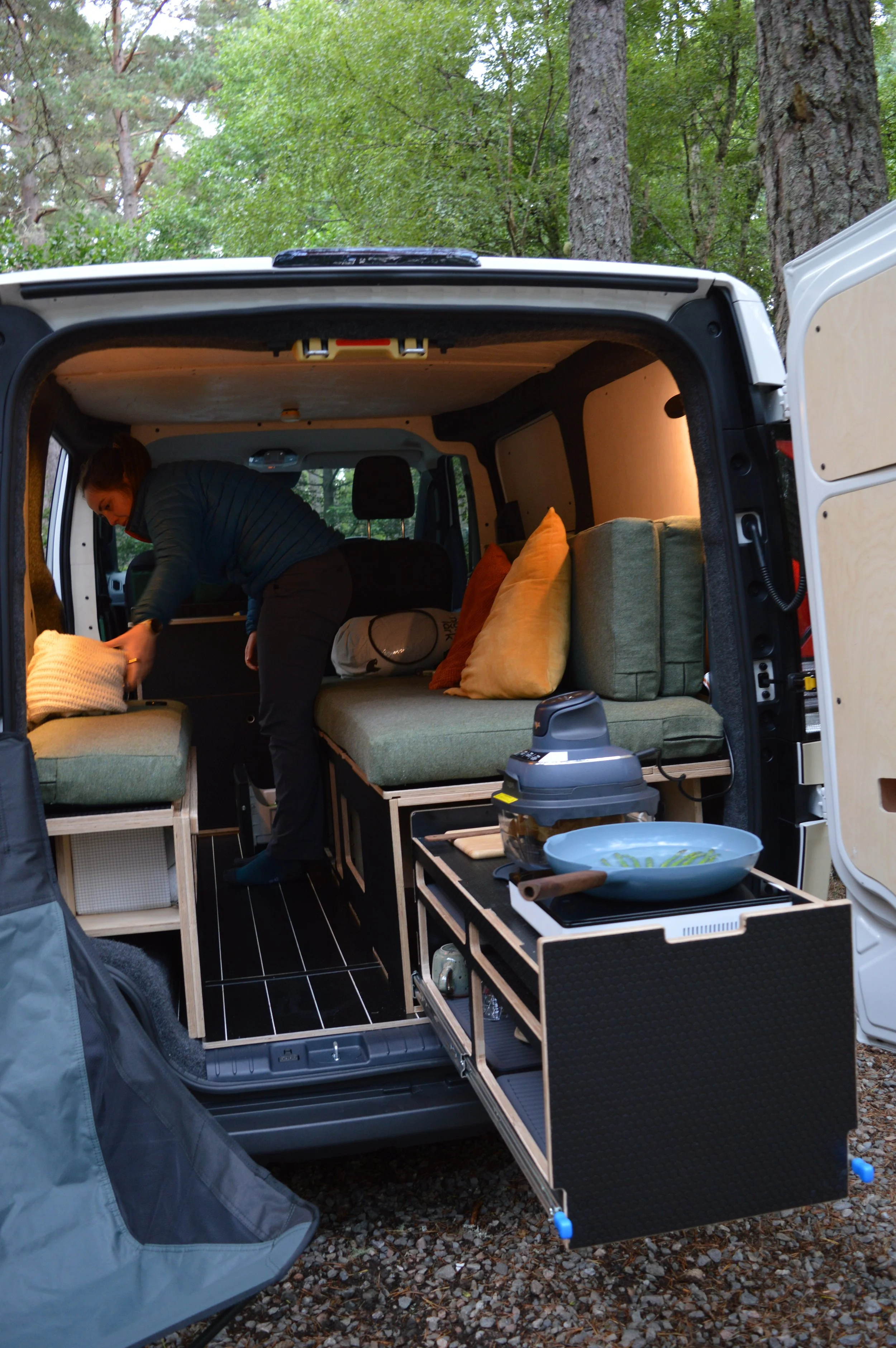 A person inside an electric campervan cooking salmon on a slide out kitchen with air fryer.