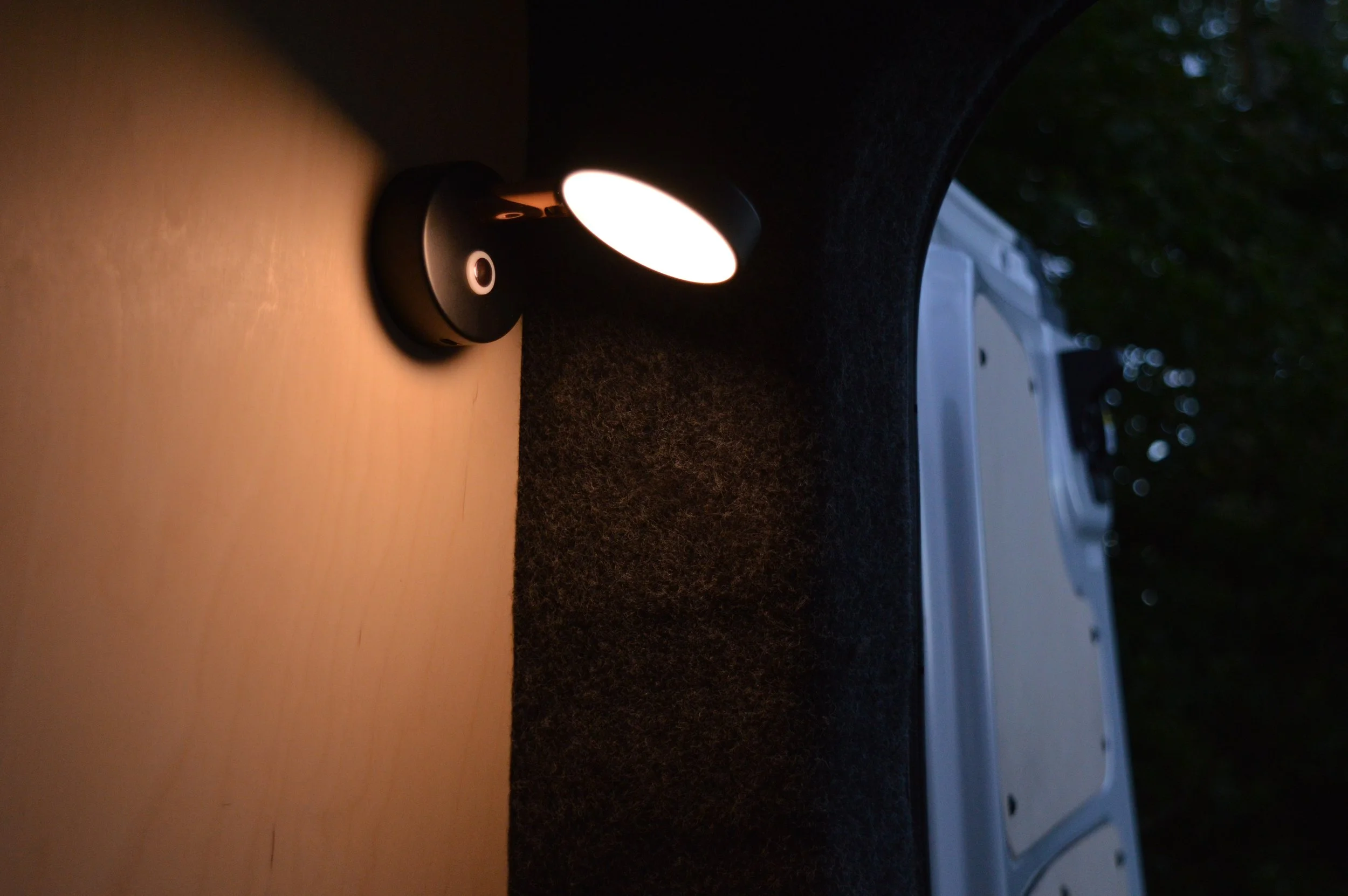 Warm reading light on birch plywood campervan wall.