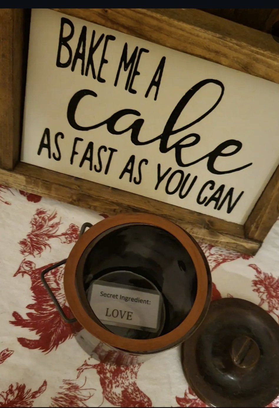 Decorative sign reading 'Bake me a cake as fast as you can' and a container with a note that says 'Secret ingredient: LOVE' inside.