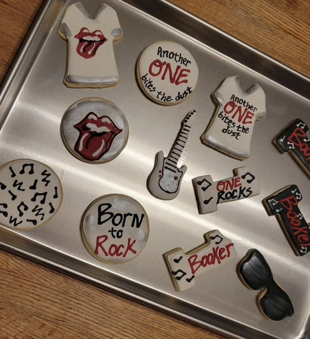 Collection of decorated cookies with rock and music themes, including lips with tongue out, guitars, sunglasses, and cookies with phrases like "Born to Rock" and "One Rocks."