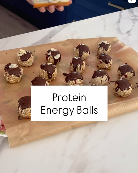 Protein energy balls topped with melted chocolate and sliced almonds, arranged on parchment paper.