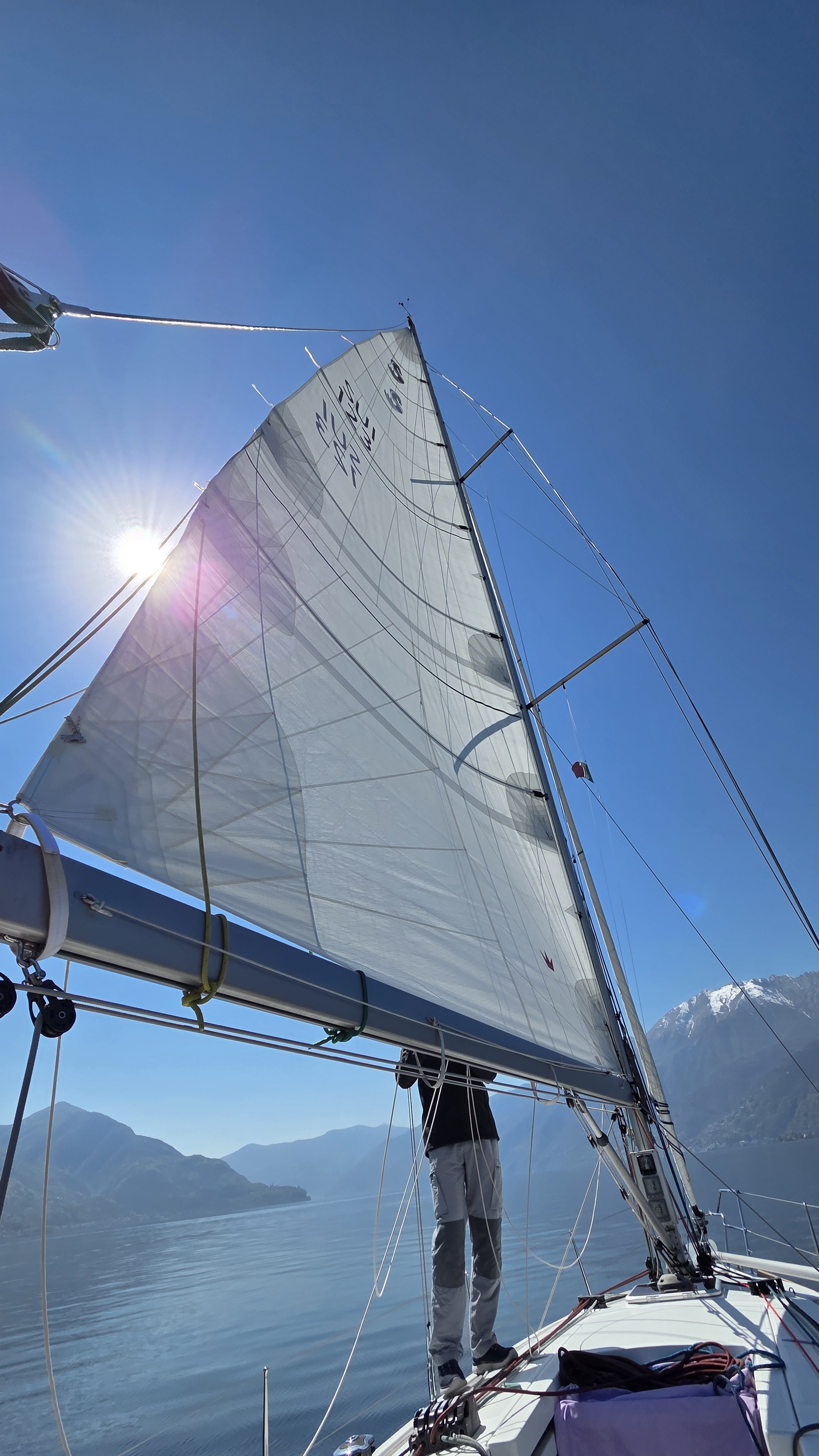 Segelboot auf einem ruhigen See, umgeben von Bergen, mit klar blauem Himmel und Sonnenschein.