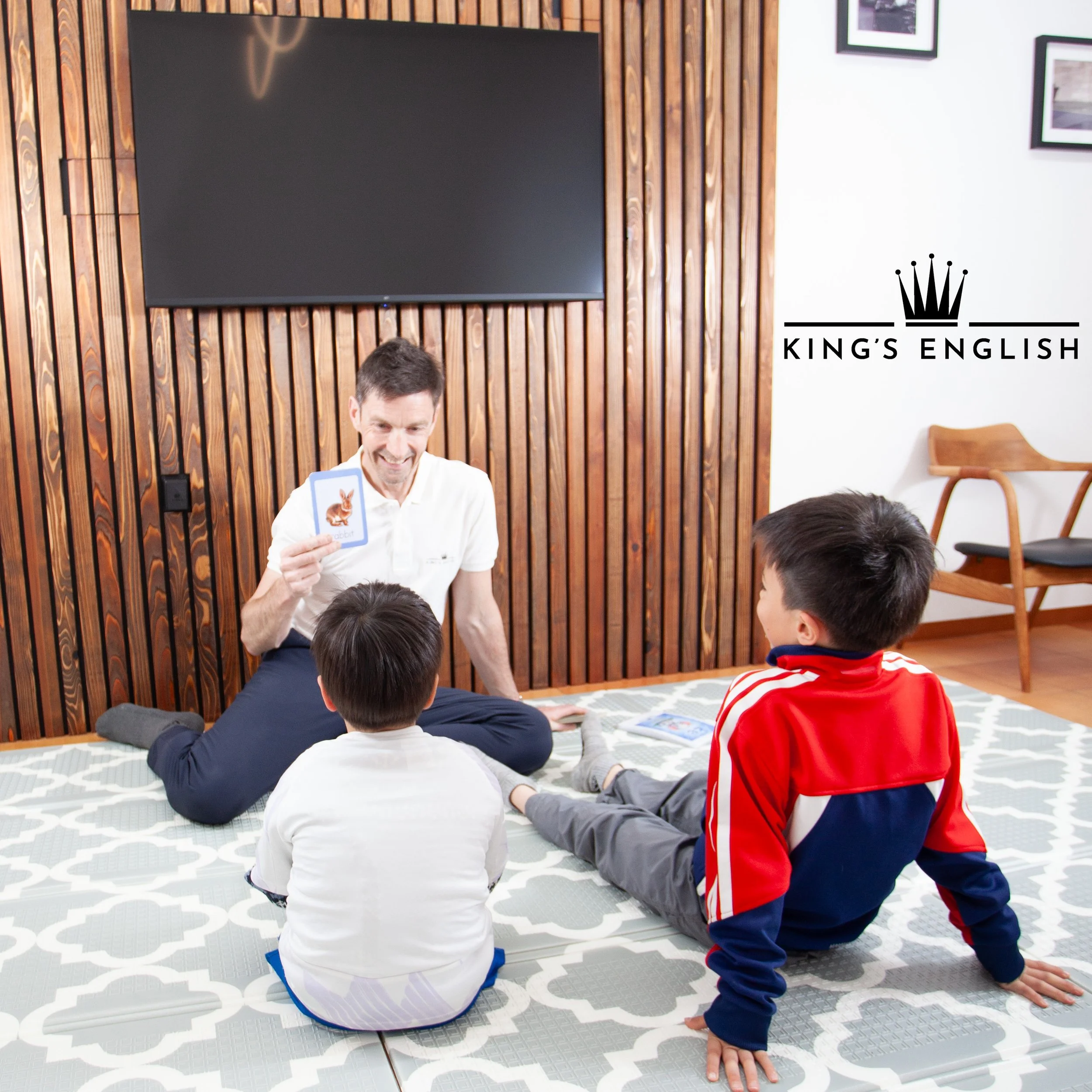 教育的な教室環境で、先生がウサギのフラッシュカードを見せながら3人の子どもと学習アクティビティを行っている子ども英会話レッスンの場面