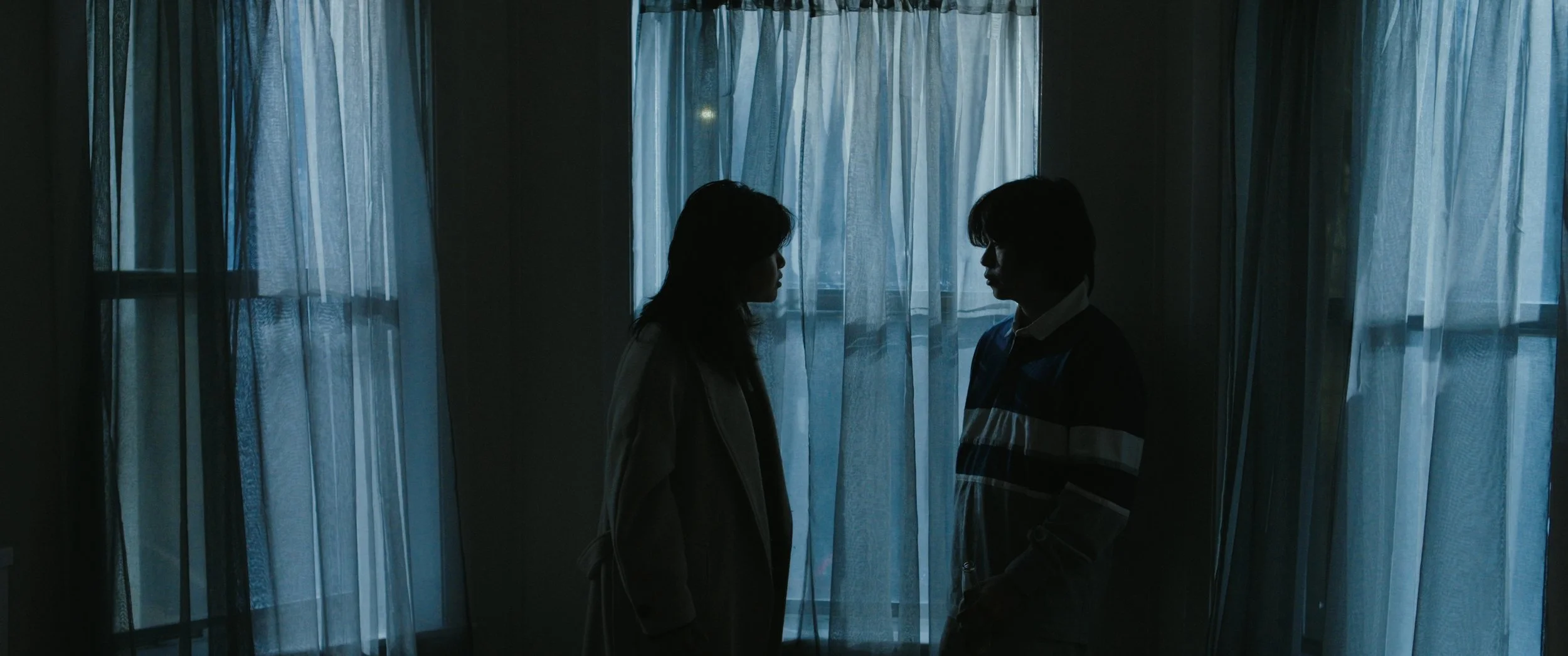 Silhouettes of two people facing each other in front of blue curtains.