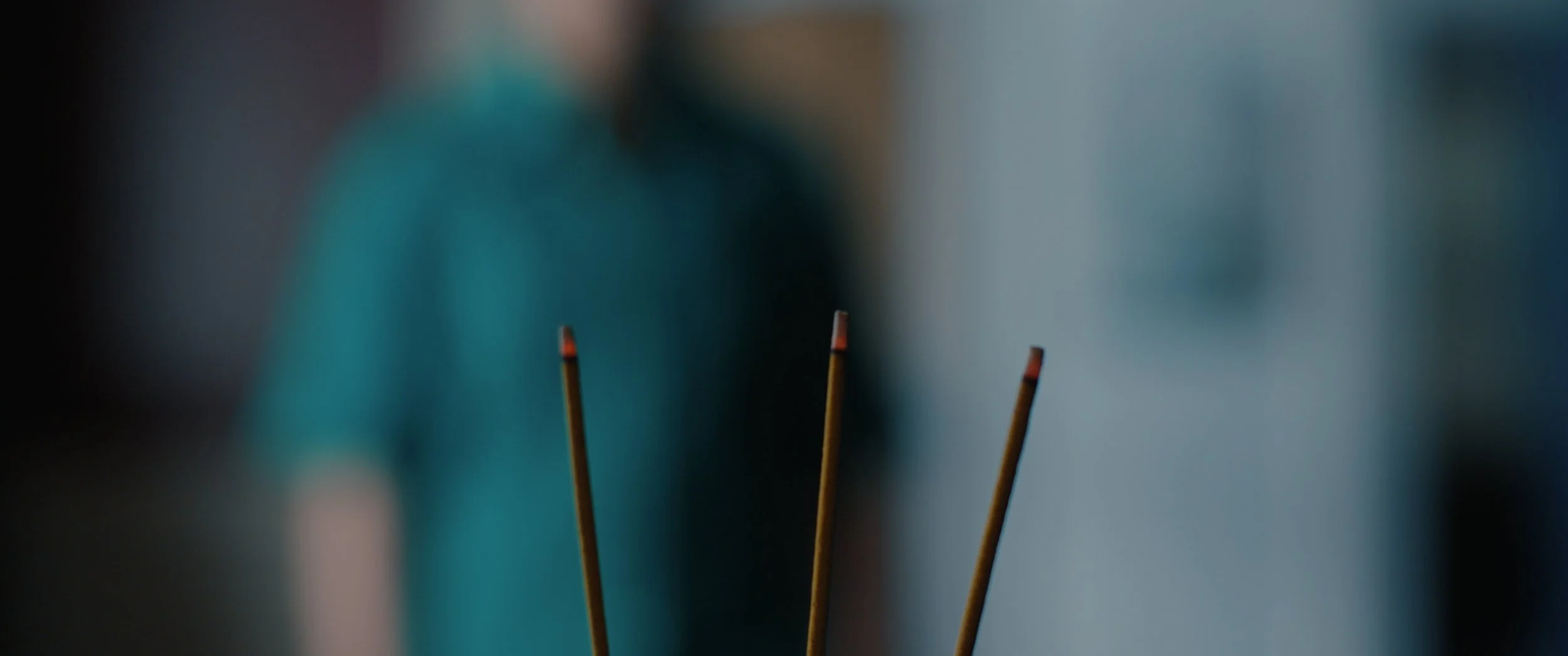 Close-up of three burning incense sticks with red tips, blurred background.