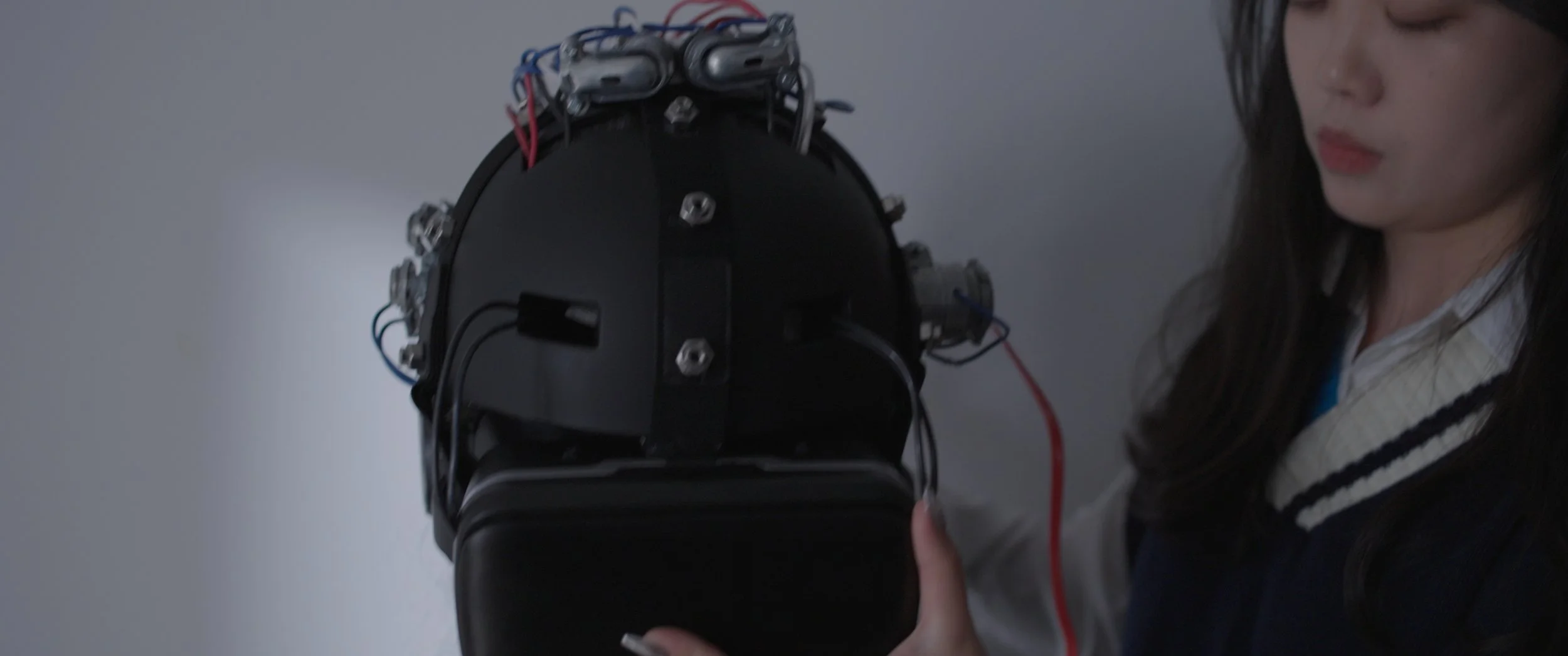 A woman examines a black device with electronic components and wires attached, possibly a scientific or technical instrument.