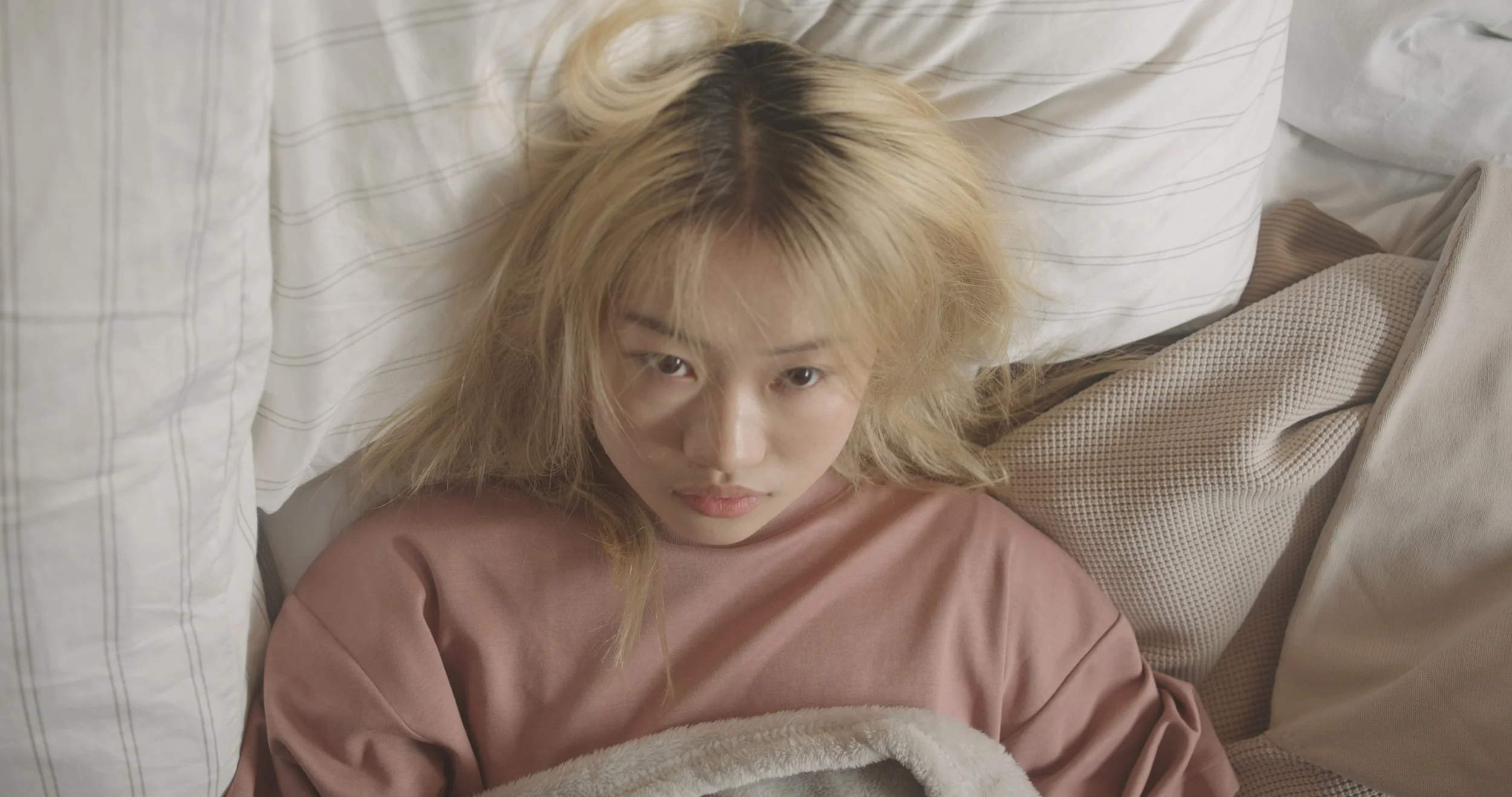 A woman with blonde hair lying on a bed, staring directly at the camera.