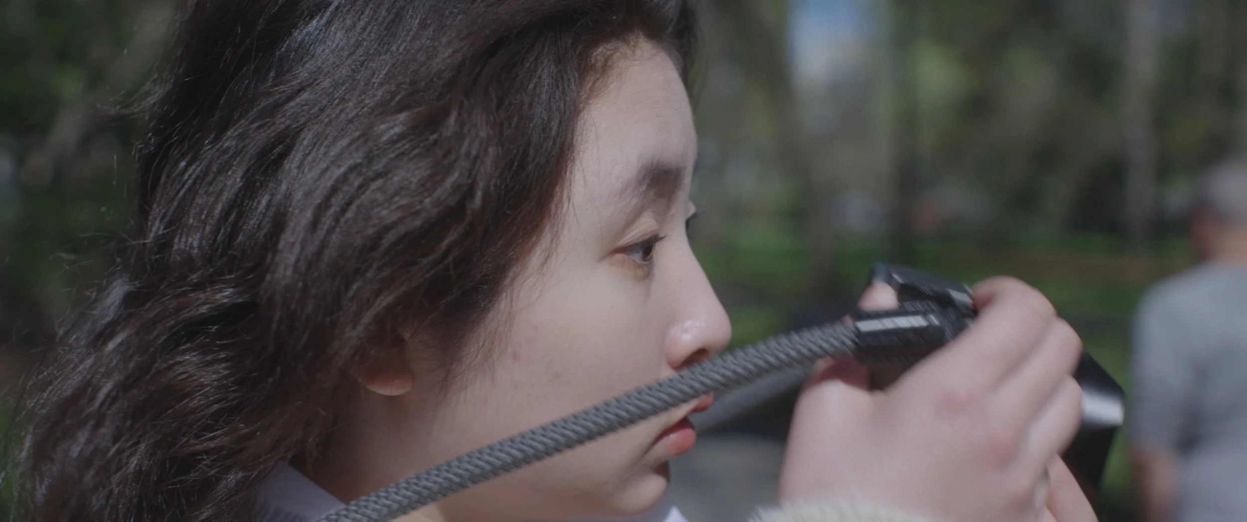 A woman with long brown hair is aiming a pistol outdoors, with focus on her face and the gun.