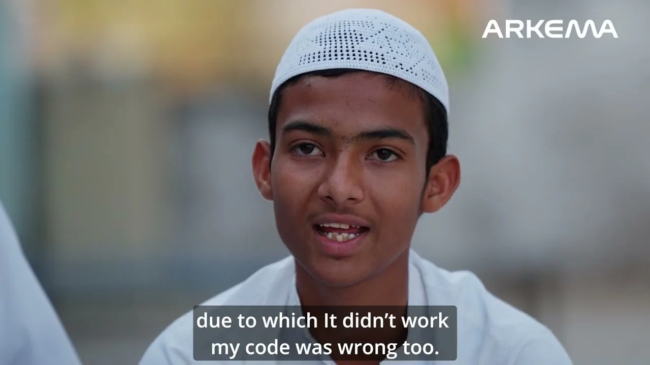 Young boy wearing a white skullcap and white shirt, speaking, with subtitles reading "due to which it didn't work my code was wrong too," outdoors, blurred background, company logo "ARKEMA" in the top right corner.