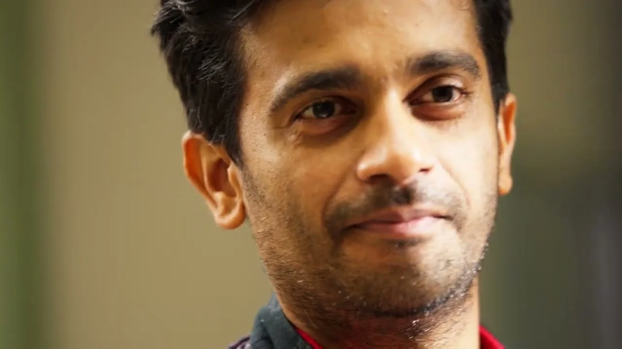 Close-up of a man with dark hair and brown skin, looking at the camera with a slight smile.