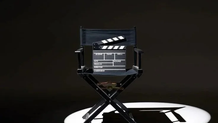 A director's chair with a clapperboard resting on it, set against a dark background with a spotlight creating a shadow.