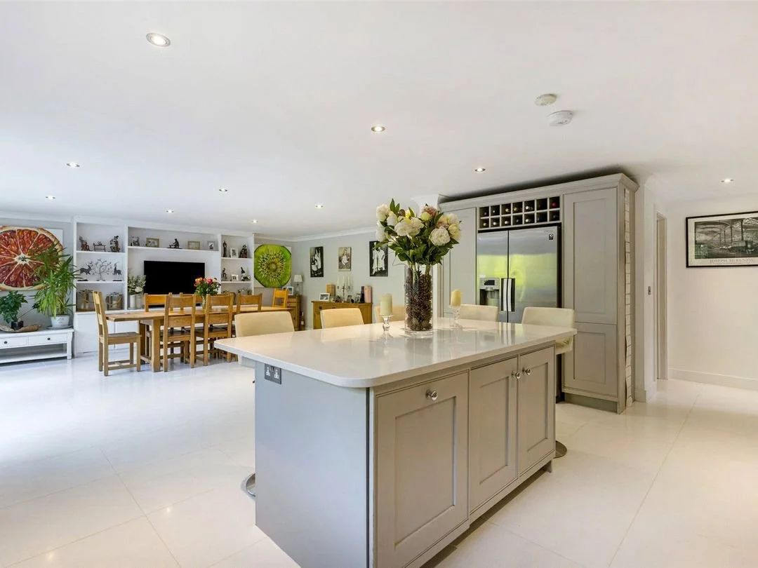 Open-concept kitchen and dining area with a large island featuring a vase of flowers, surrounded by dining tables, chairs, built-in shelves, and artwork.
