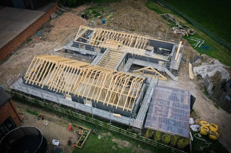 A house under construction with wooden framing and scaffolding, viewed from above.