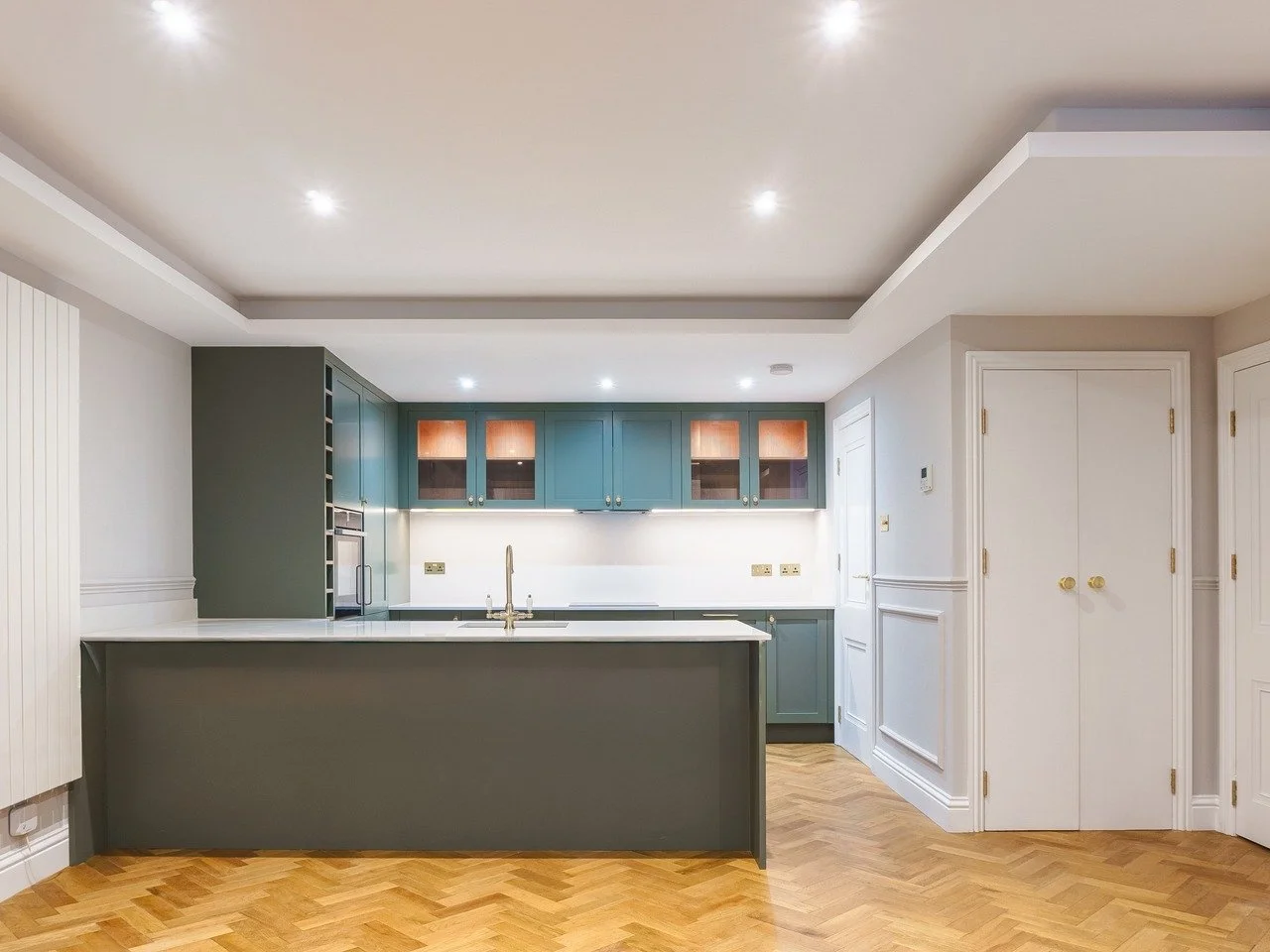 Modern kitchen with blue cabinets, white countertops, wooden floor, and ceiling lights.