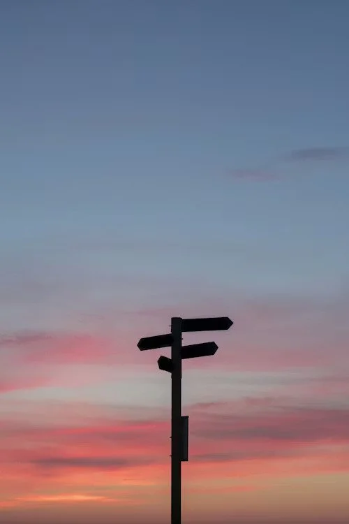 Silhouette of a street sign against a colorful sunset sky with shades of pink, orange, and blue.