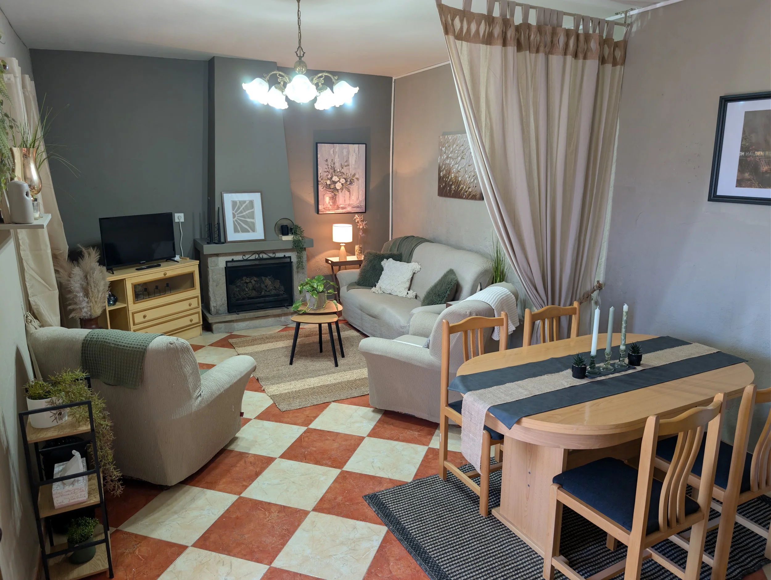 Living room with a fireplace, TV, beige sofas, a dining table with chairs, and decorative plants.