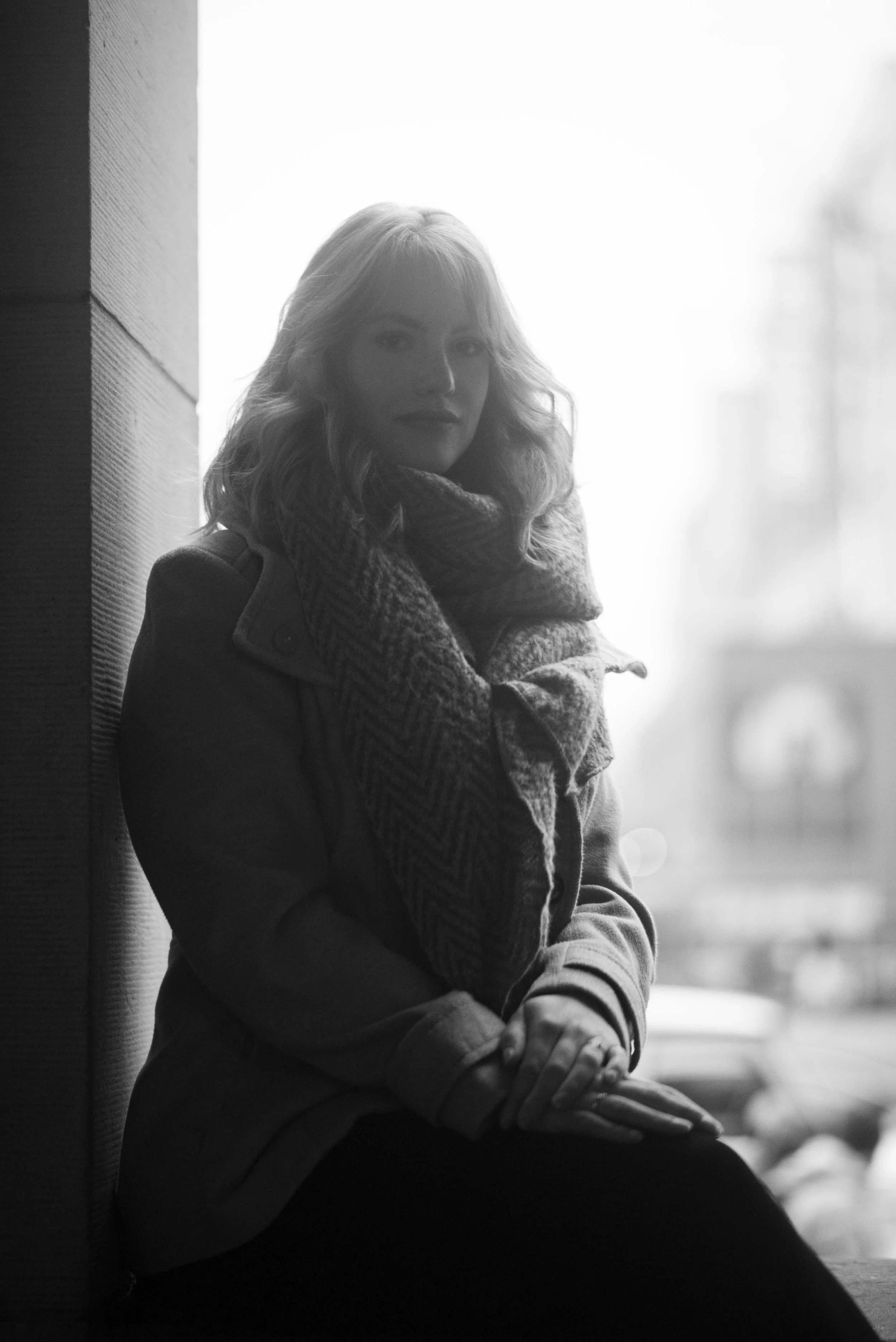 Sfeervol zwart-wit portret van een vrouw die leunt in een lichte opening in de stad.