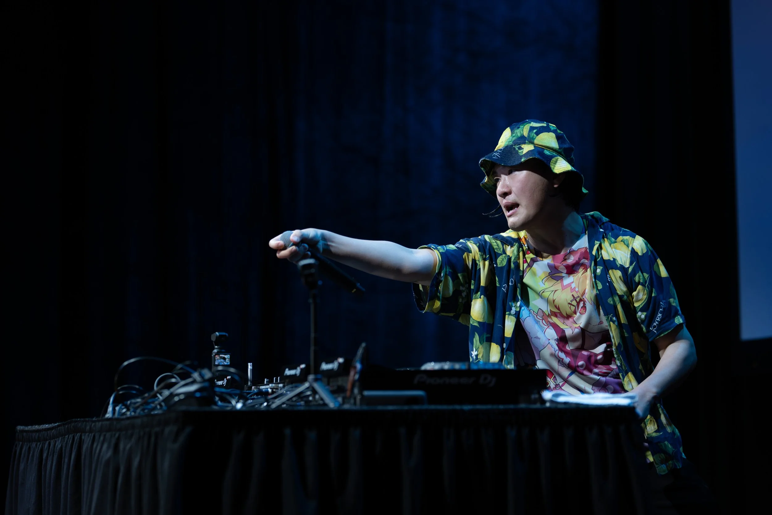 Eventfotografie van een DJ in een kleurrijke outfit die optreedt op een donker poppodium.