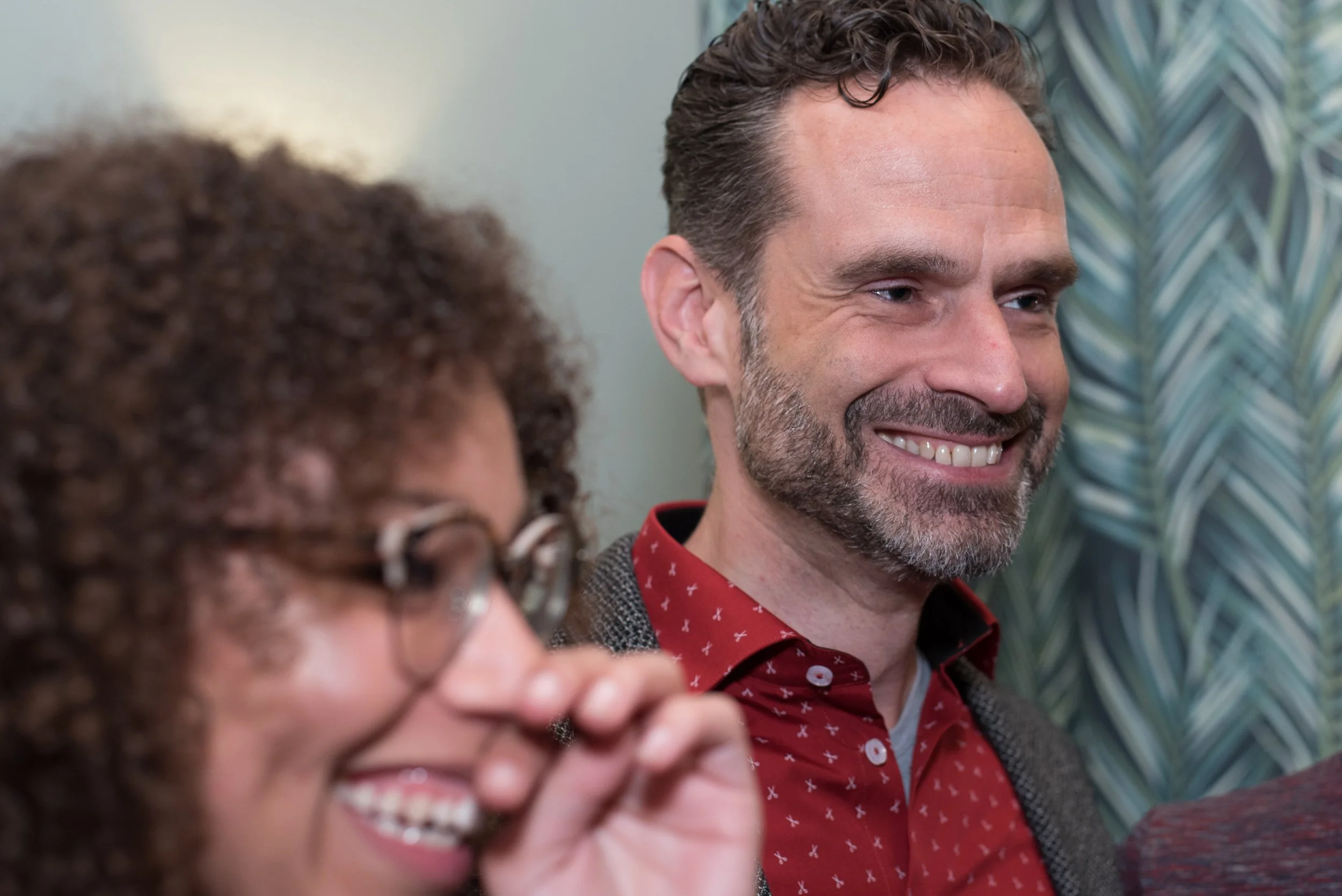 Glimlachende man met baard in een rood overhemd tijdens een feestelijke evenementenborrel.