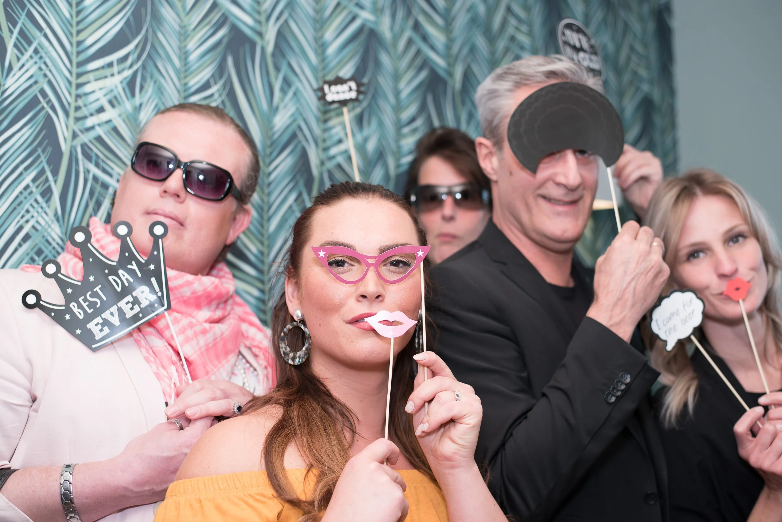 Gezellige groepsfoto van gasten met feestelijke brillen en snorren in een fotobooth.