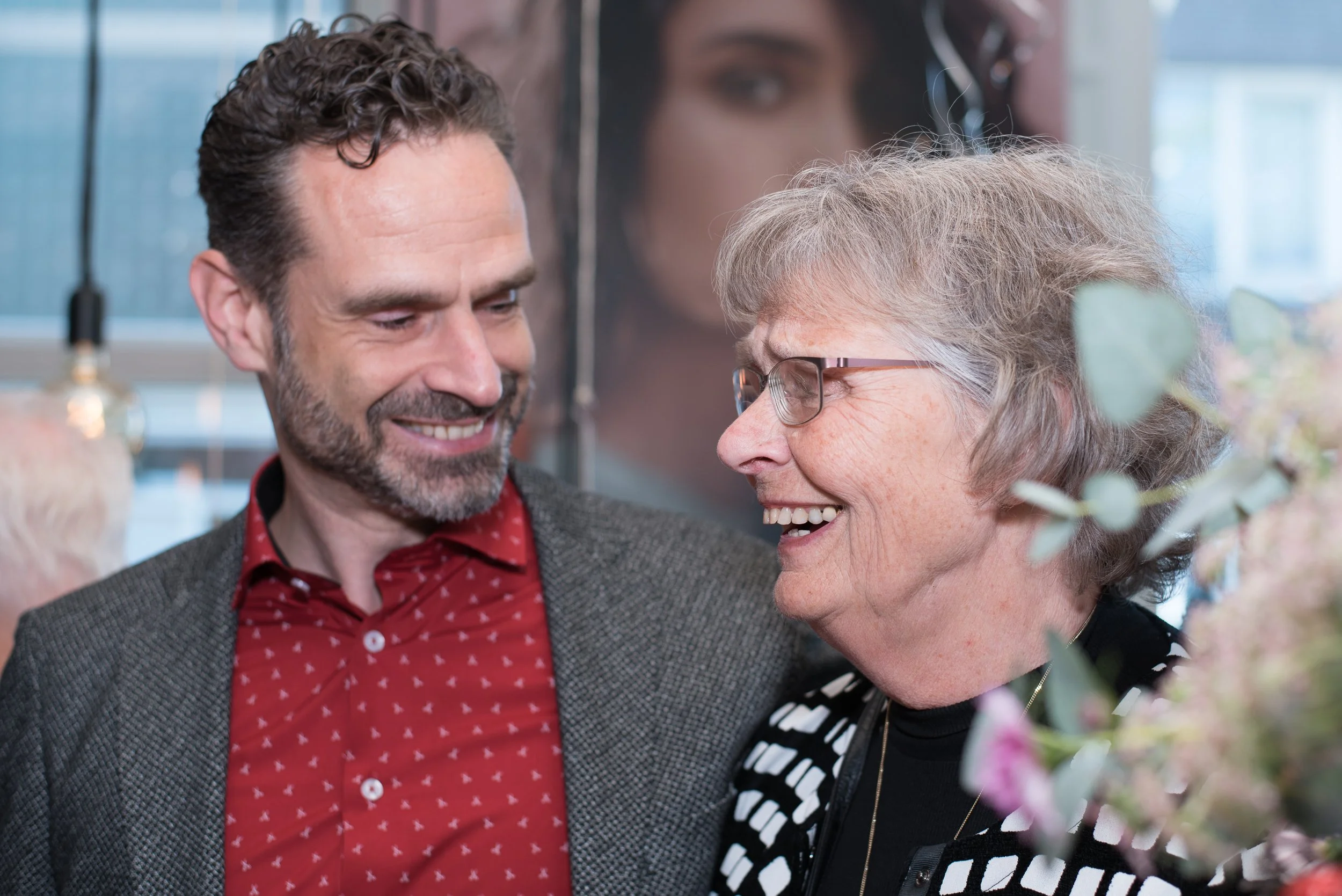 Spontane momentopname van een man en een oudere vrouw die samen lachen tijdens een borrel.