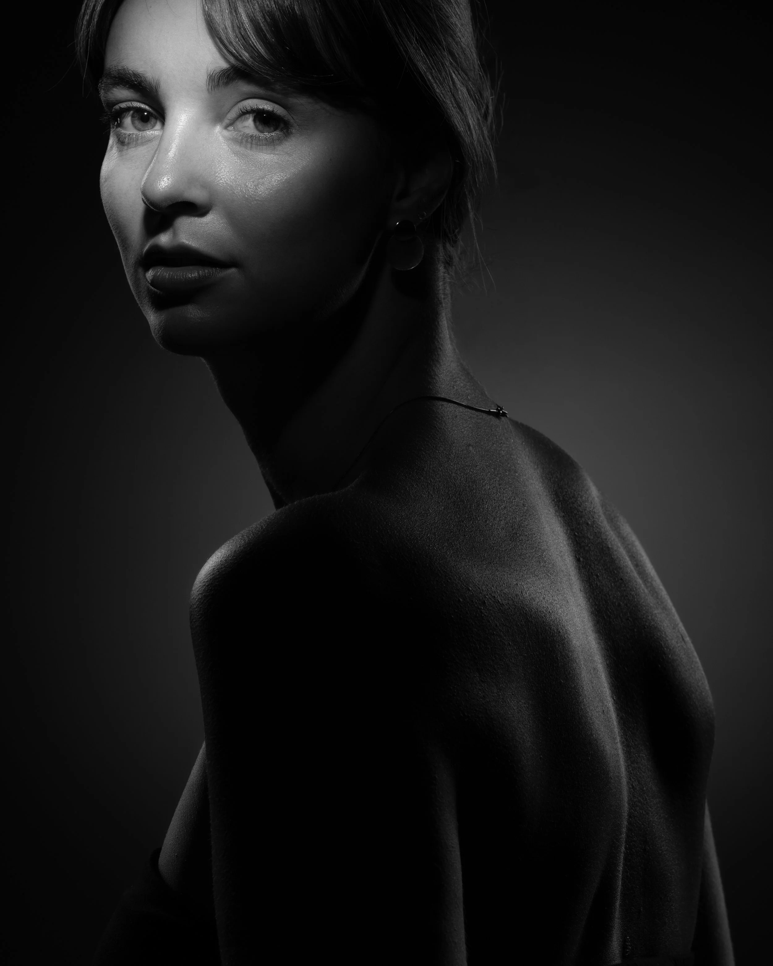 Artistiek zwart-wit portret in clair-obscur stijl van het zijprofiel van een jonge vrouw.