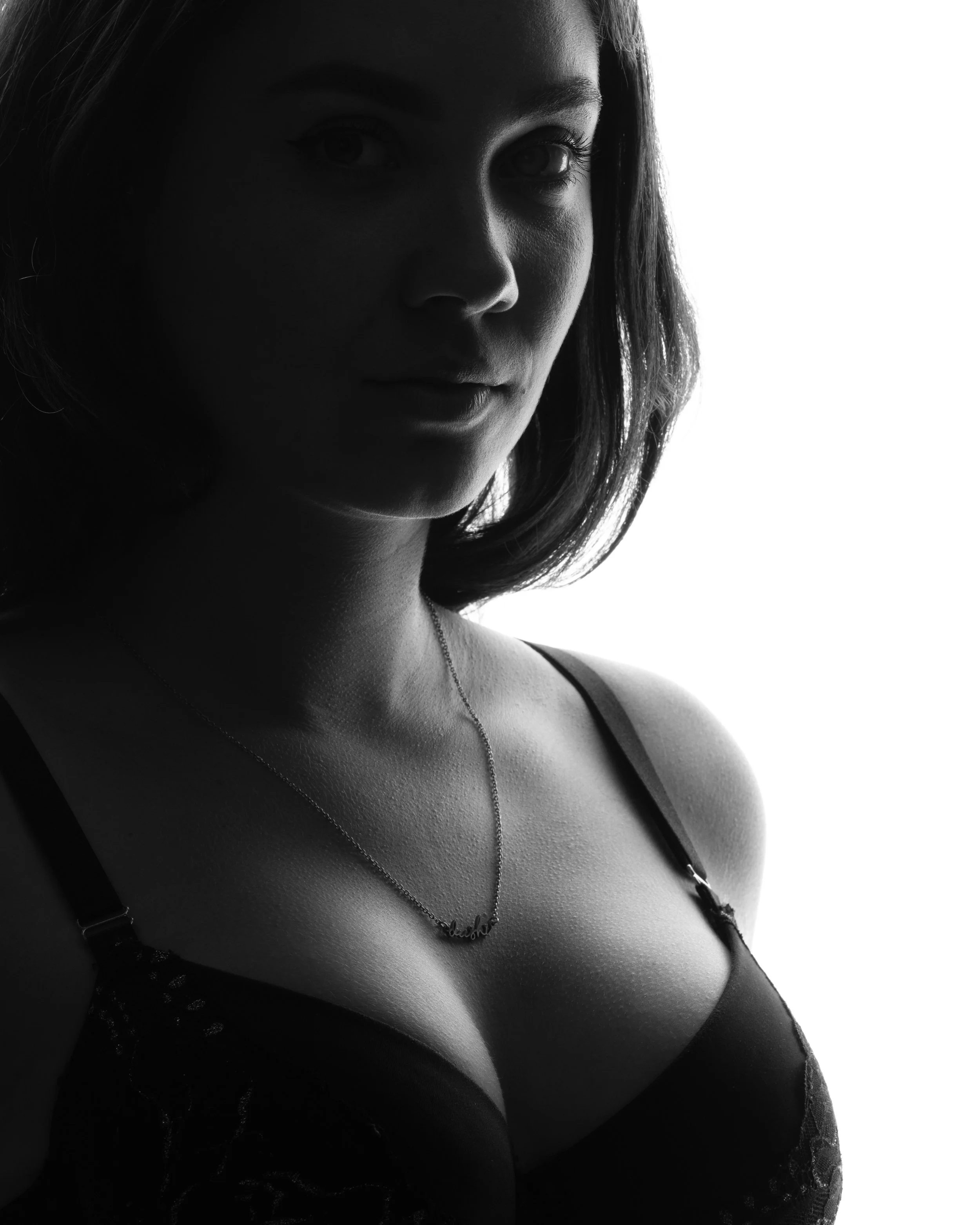 Low-key zwart-wit boudoir portret van een vrouw met de nadruk op een subtiele halsketting en schaduwen.