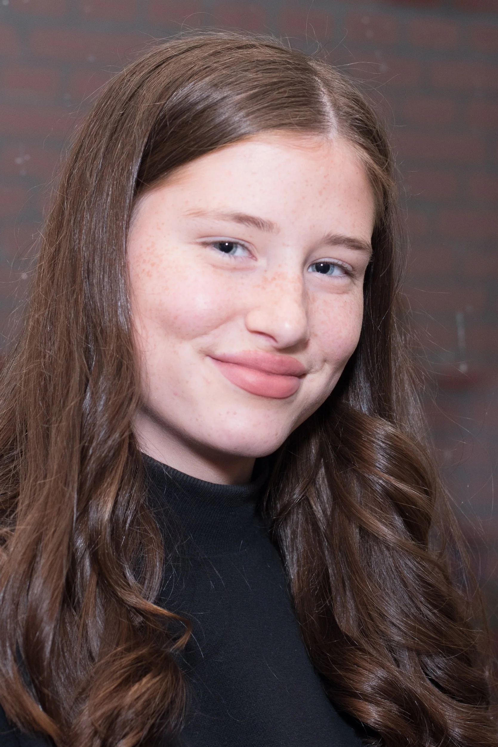 Portret van een glimlachend jong meisje met lang bruin haar tijdens een bijeenkomst of feest.