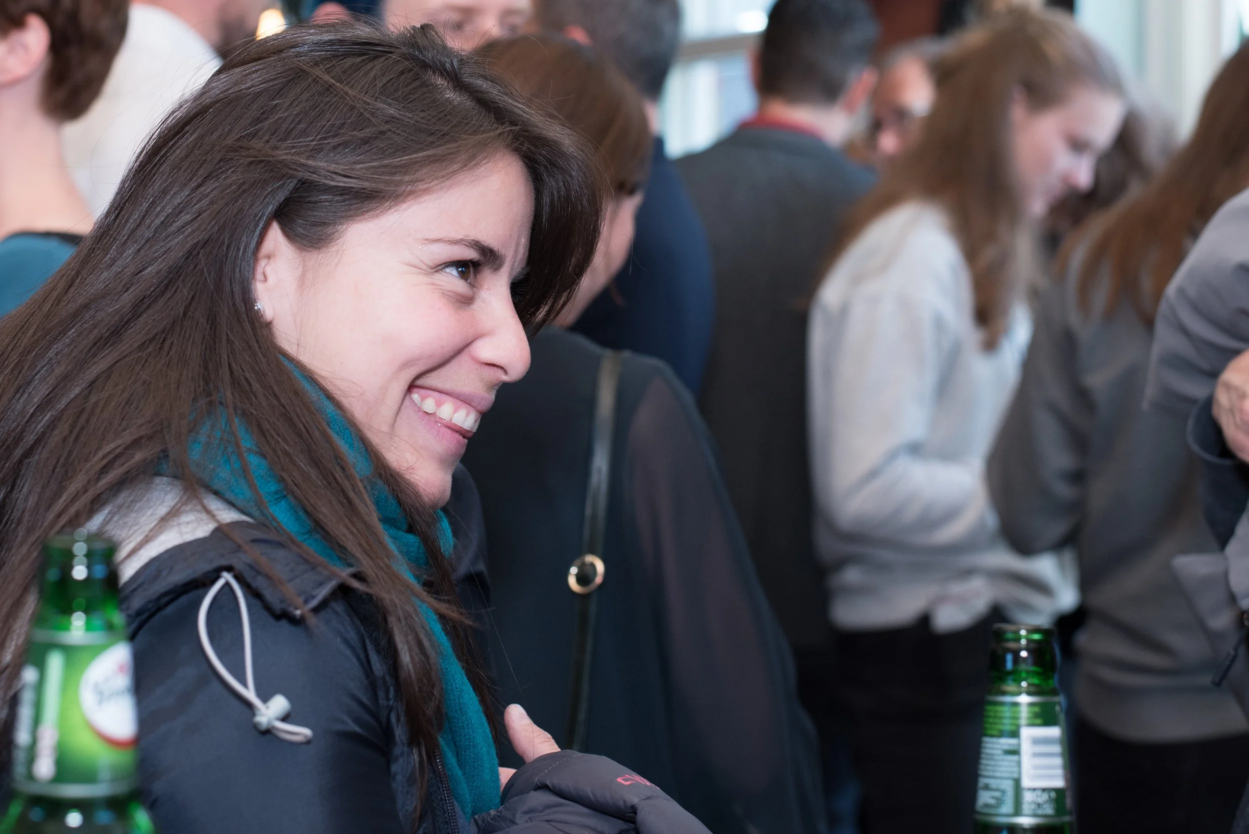 Spontaan portret van een lachende vrouw met een groenblauwe sjaal tijdens een druk evenement.