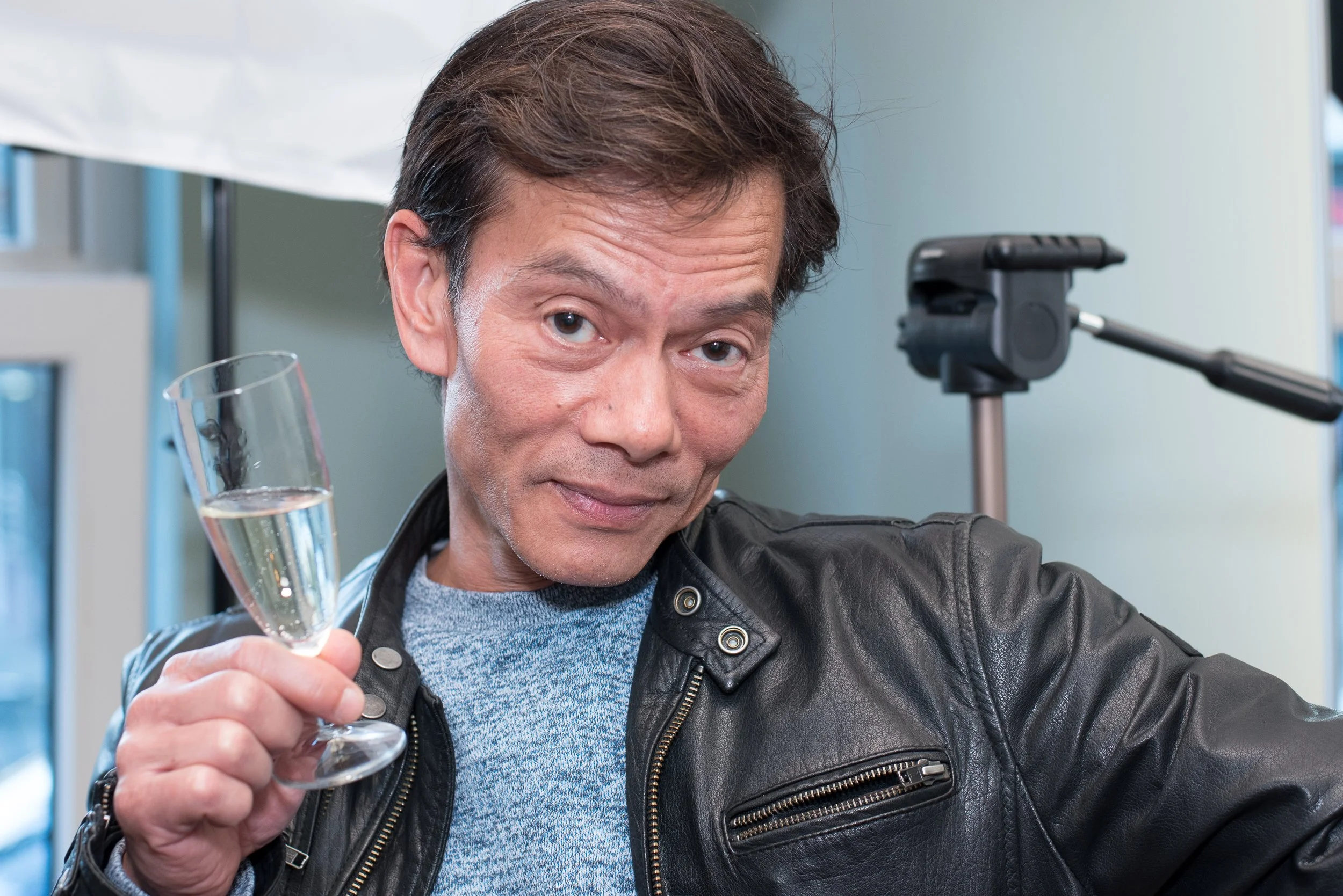 Vrolijke man in een leren jas die proost met een glas champagne op een evenement of feest.
