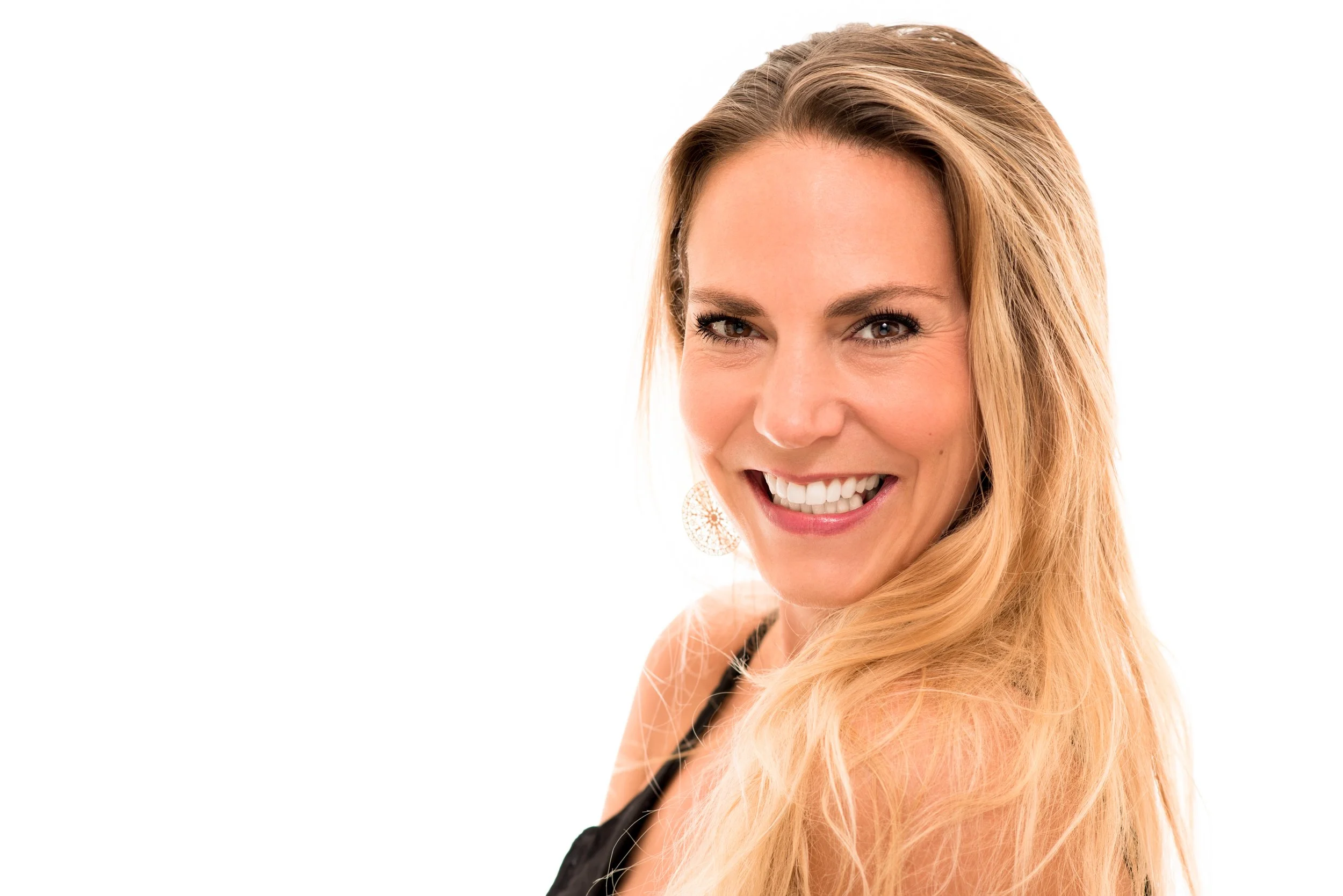 Frisse, lichte headshot van een breed glimlachende blonde vrouw tegen een helderwitte achtergrond.