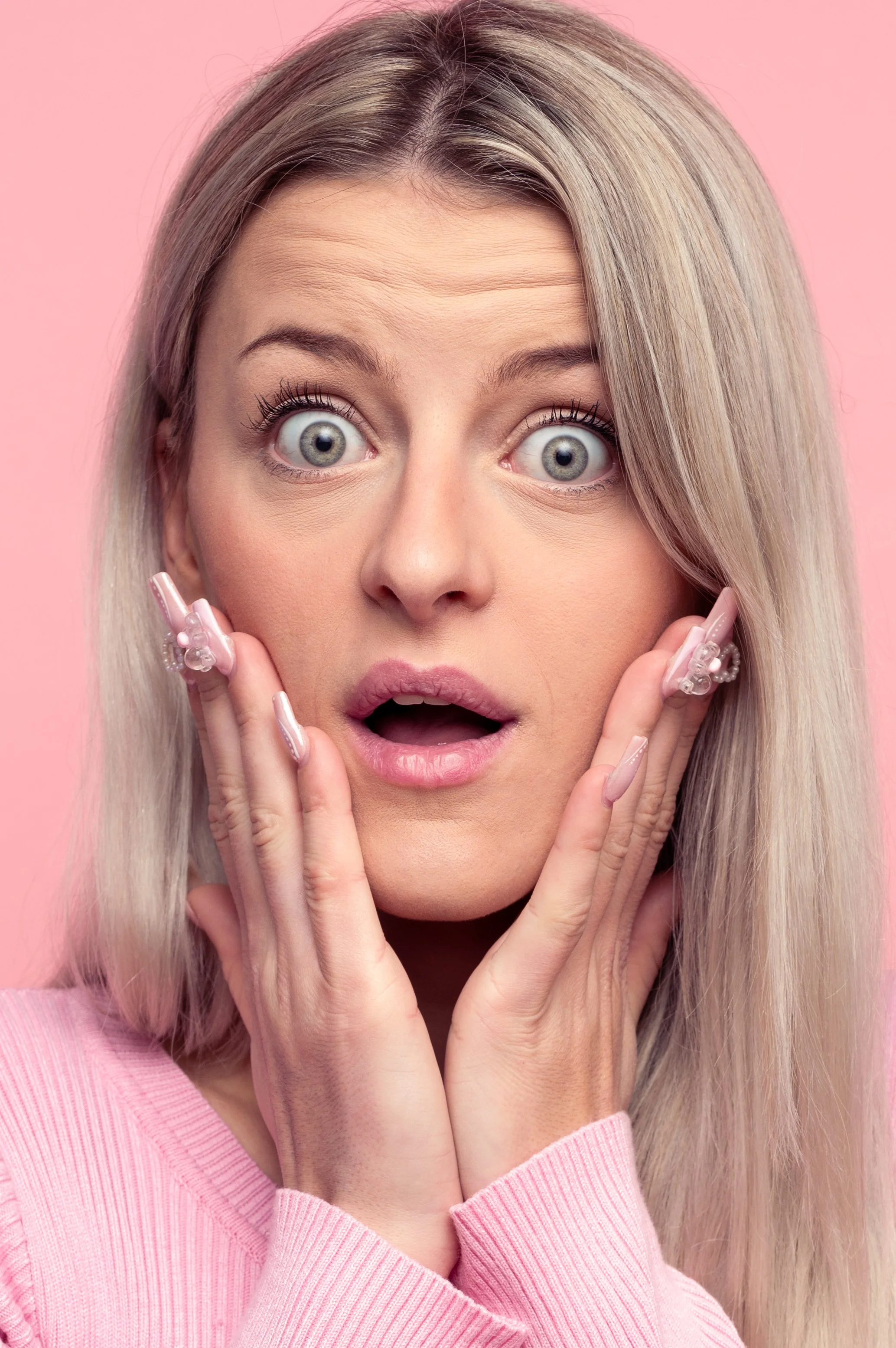Spontaan en expressief portret van een blonde vrouw met een verraste gezichtsuitdrukking in een roze trui.