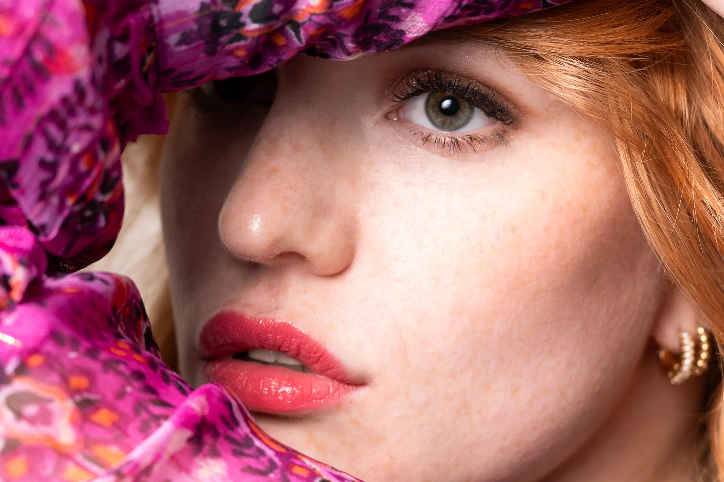 Intieme close-up van een vrouwelijk gezicht omringd door een kleurrijke, roze kanten doek.