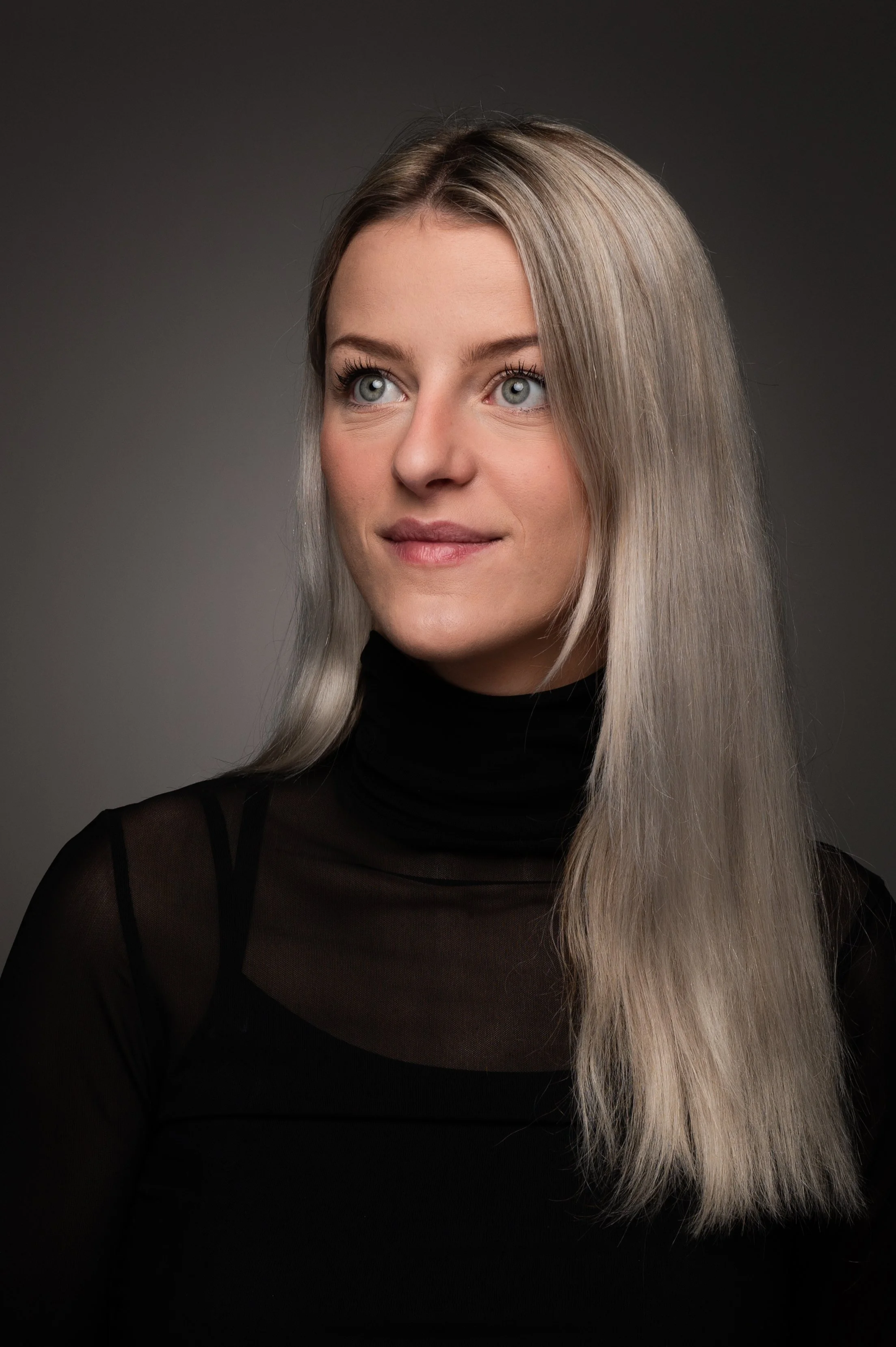 Klassiek studioportret van een vrouw met een zwarte coltrui tegen een grijze studioachtergrond.