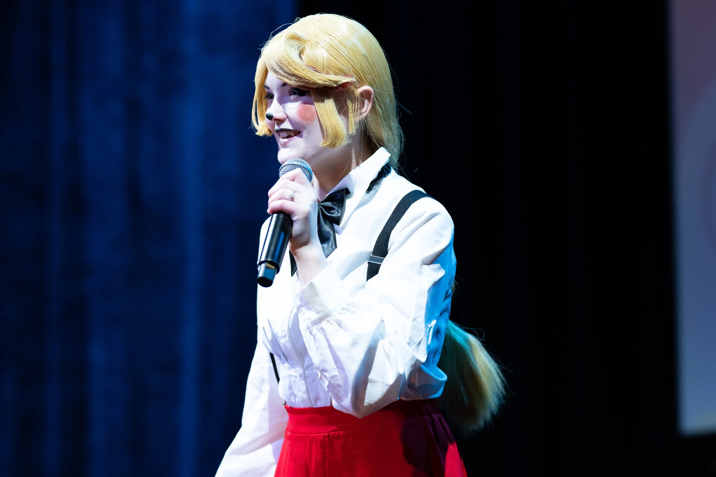 Eventfotografie van een blonde zangeres in een wit overhemd met een microfoon op het podium. presentatie.
