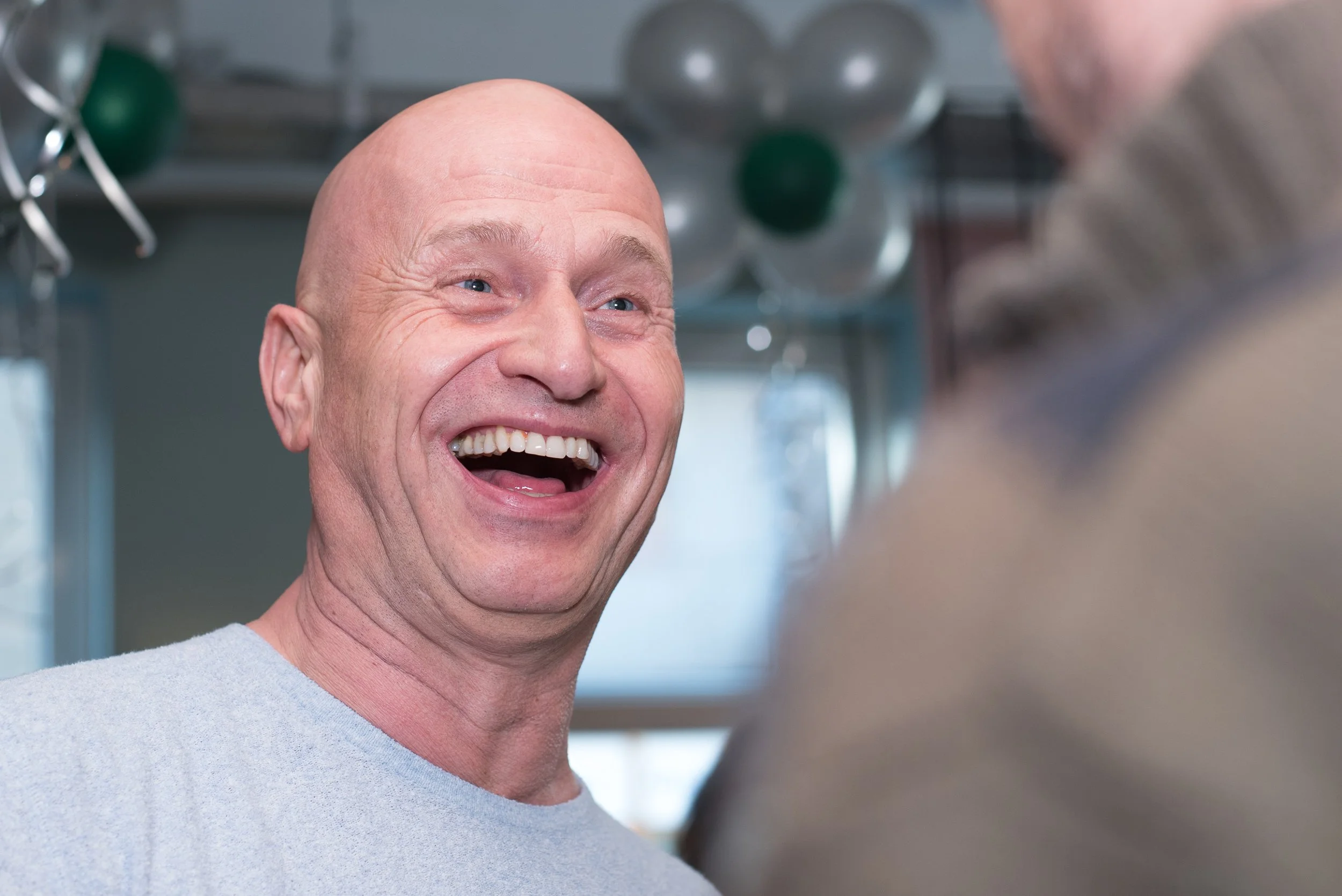 Portret van een hard lachende, kale man tijdens een gezellige netwerkborrel of evenement.