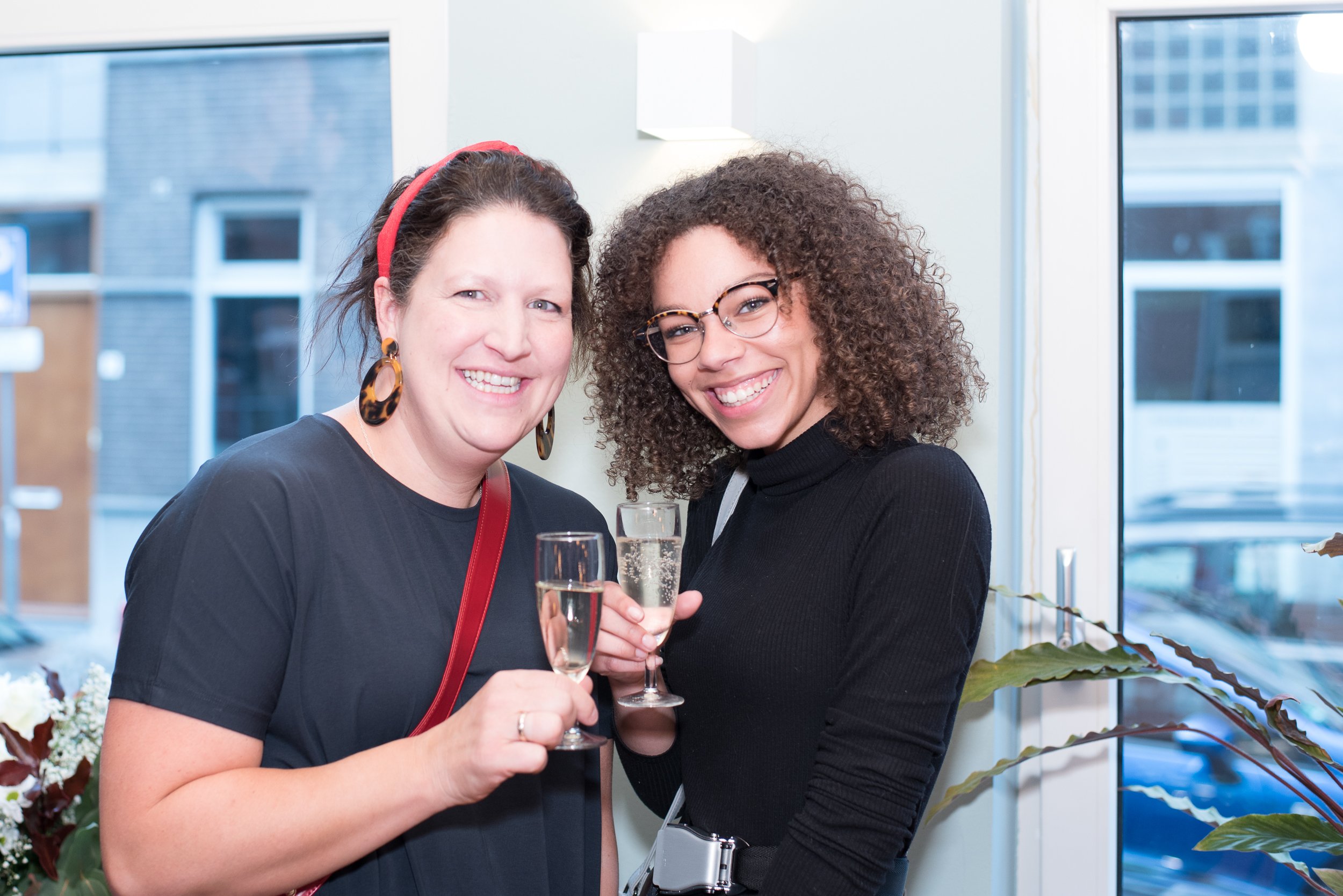 Eventfotografie van twee lachende vrouwen die proosten met een glas champagne op een feest.